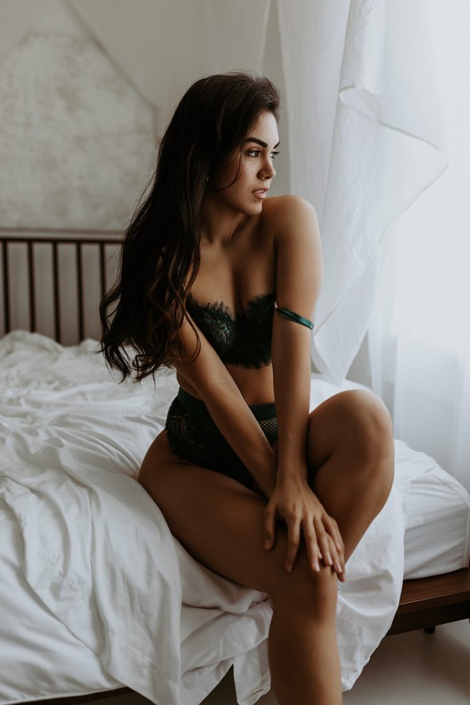 Woman in emerald green lace lingerie posing on a bed for her boudoir session in Minnesota.