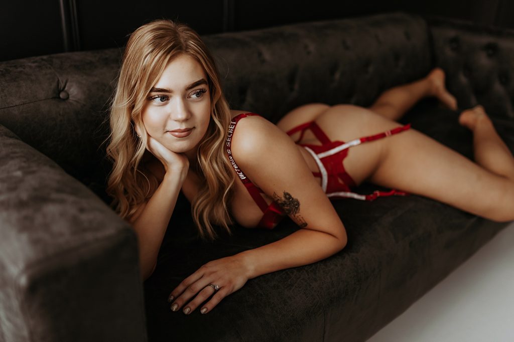 Woman in red lingerie lying across a brown leather couch. 