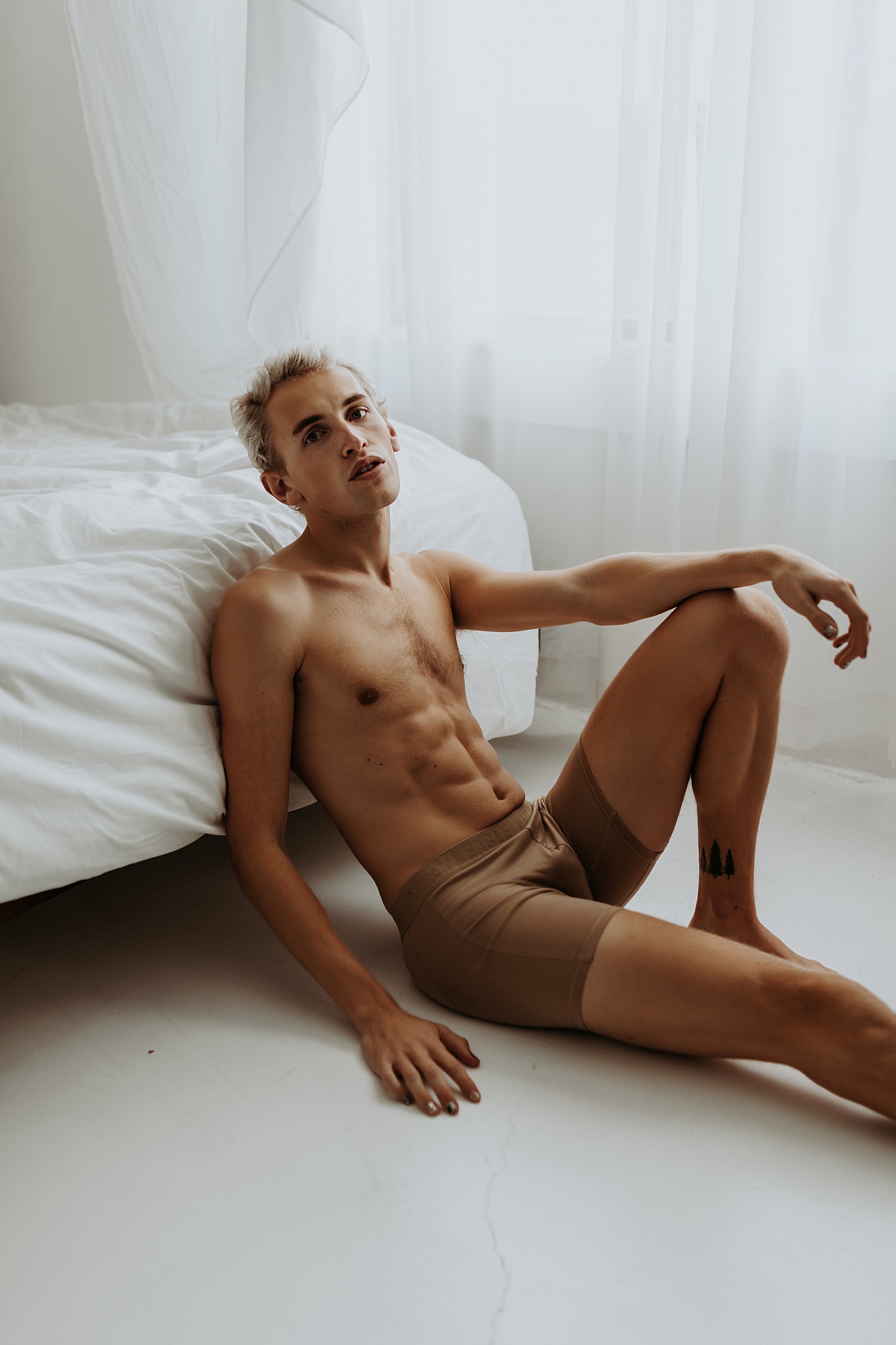 Blonde man in underwear sitting against a bed for his male boudoir session at Minneapolis studio. 
