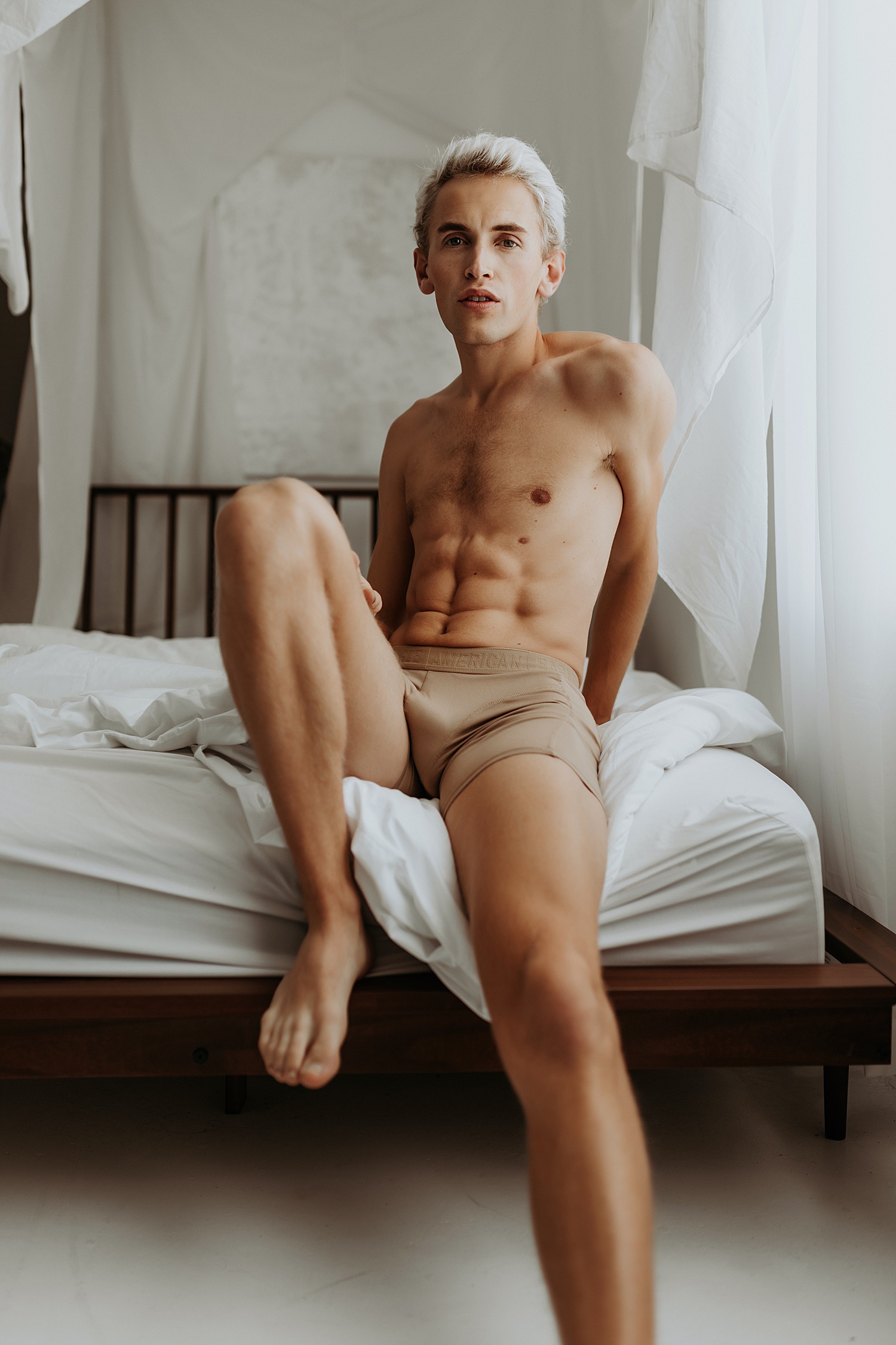 Man sitting on a bed in underwear for a studio boudoir session in Minnesota.