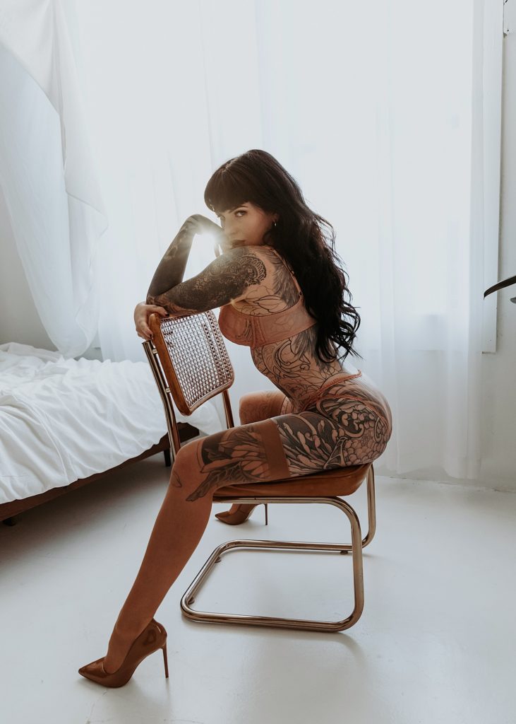 Tattooed woman sitting on a chair in a boudoir studio in Minnesota.