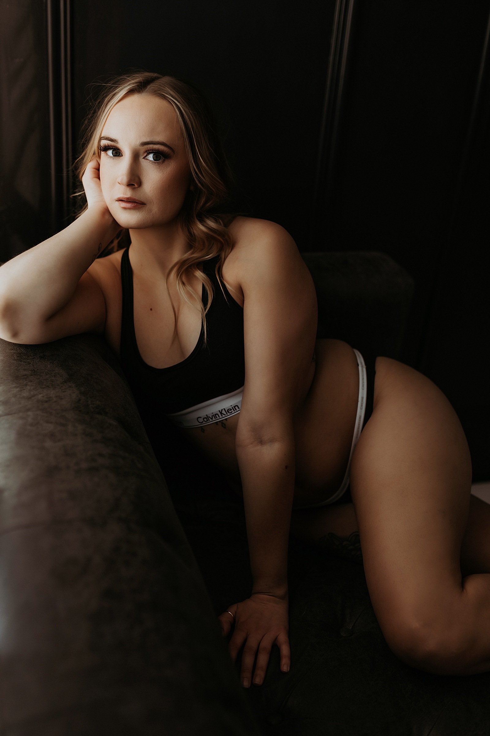 Woman wearing a two piece lingerie Calvin Klein set while sitting on a leather couch