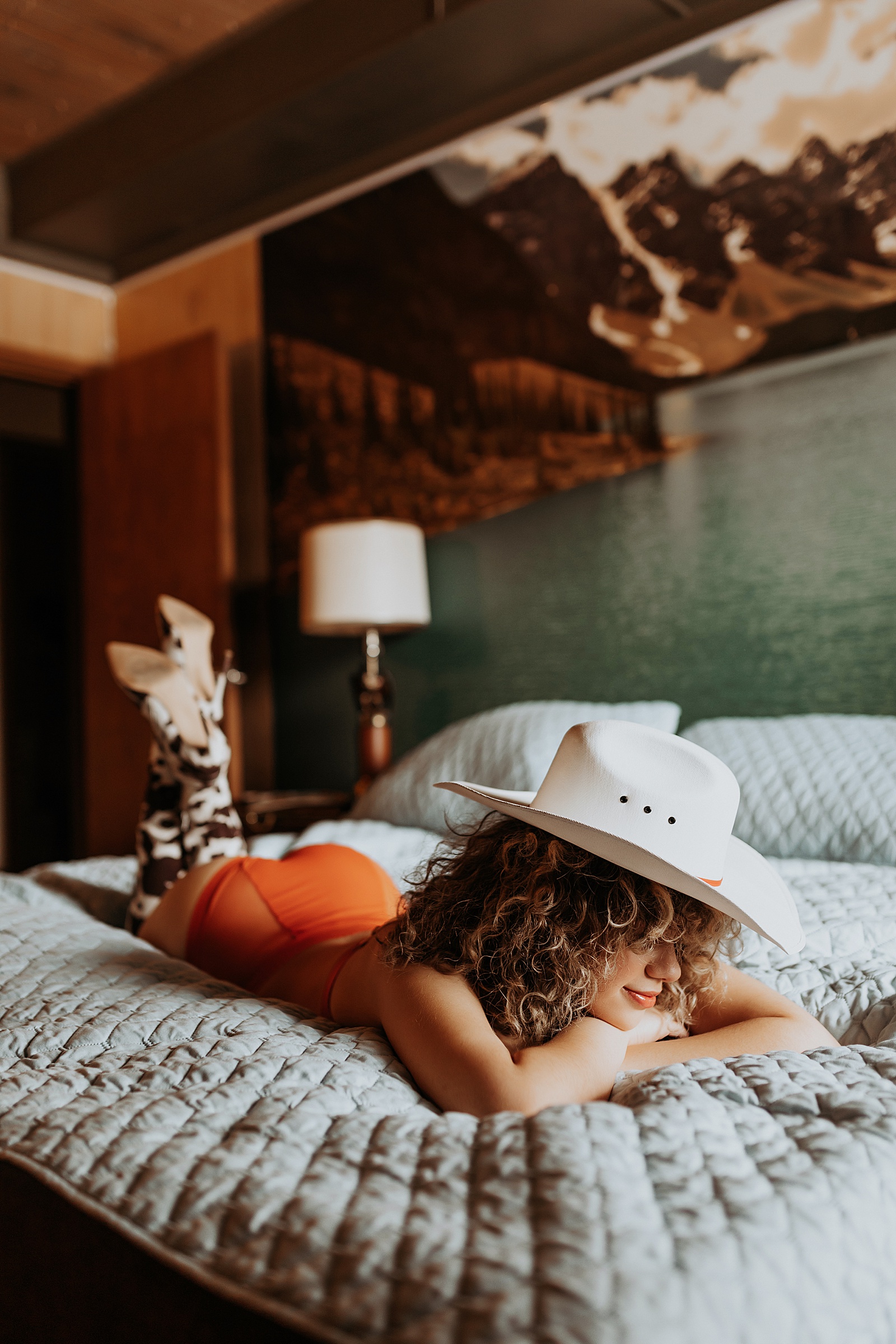 Curly hair woman with a cowboy hat lying across a bed in lingerie 