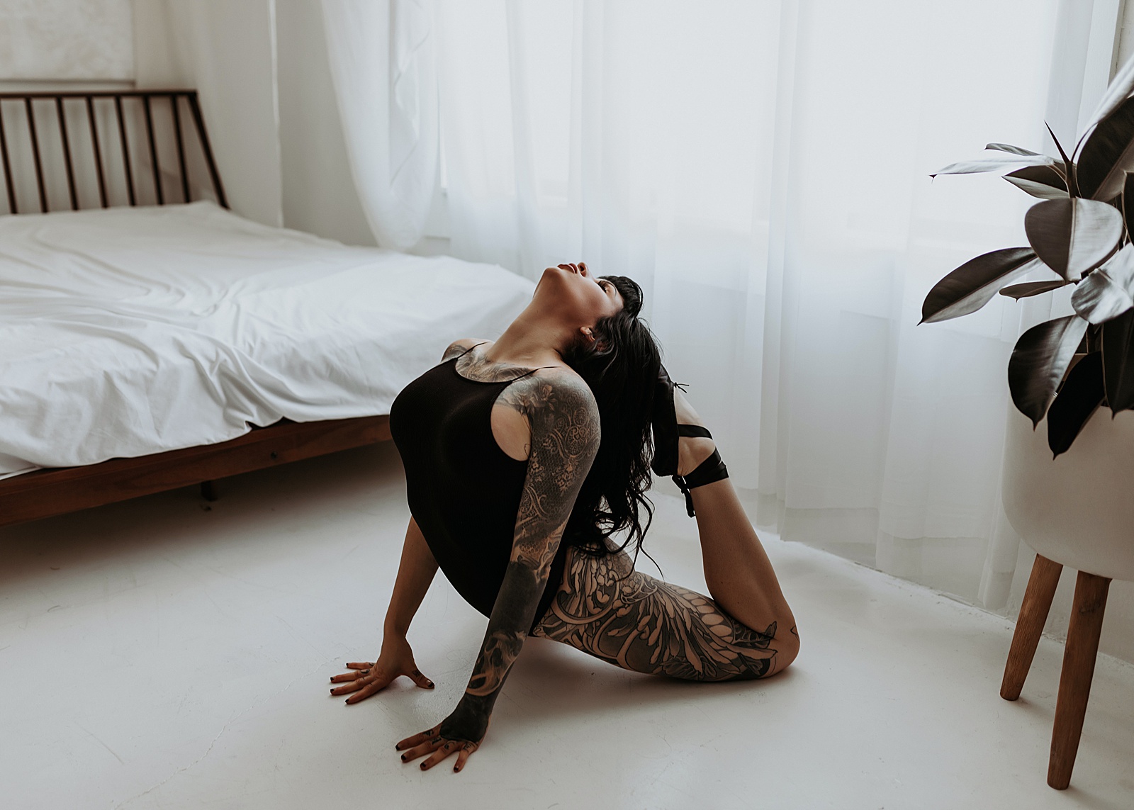 Woman with tattoos kneeling on boudoir studio floor in black bodysuit lingerie