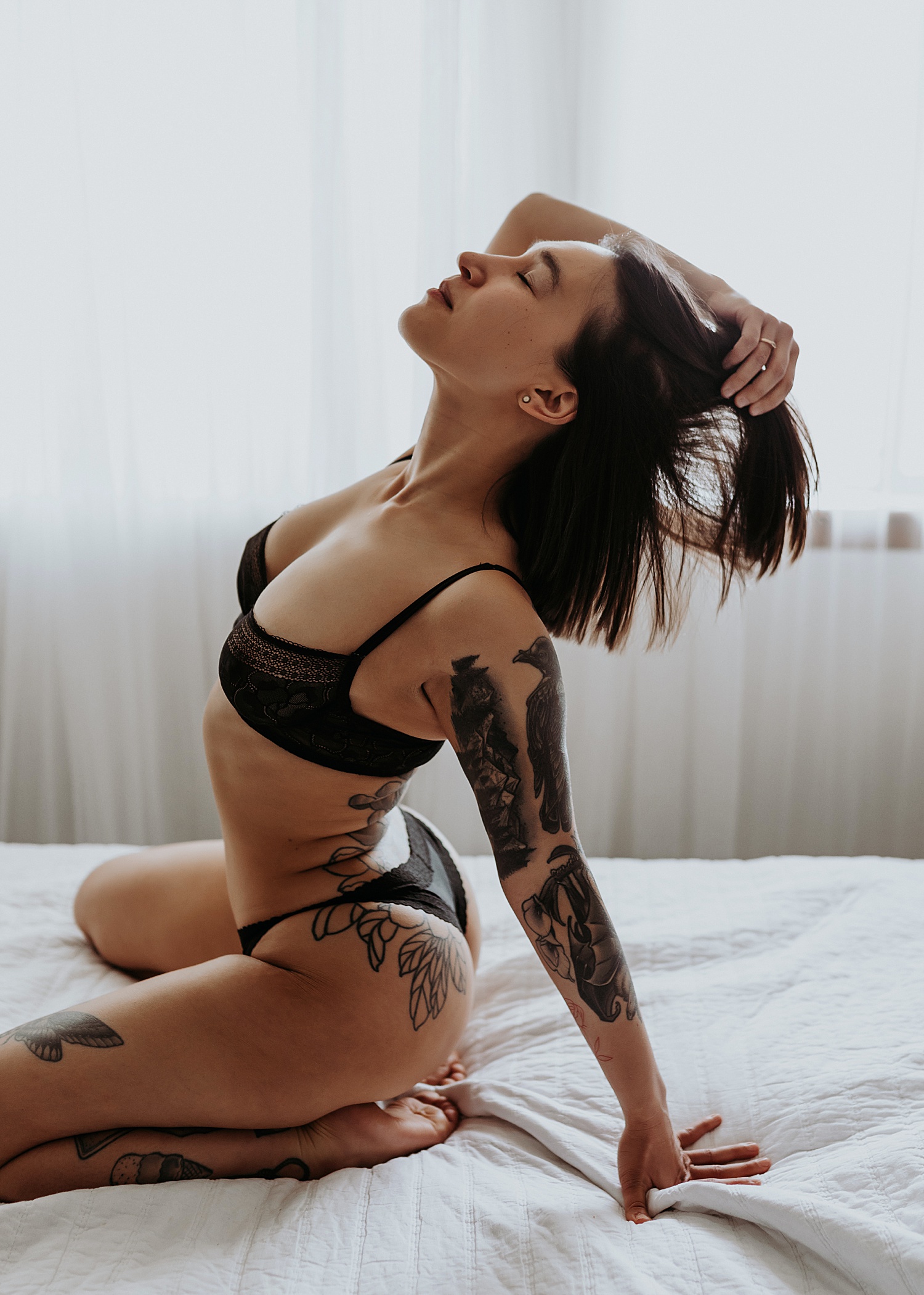 Woman kneeling on a bed in a black bra at sexy photo shoot 