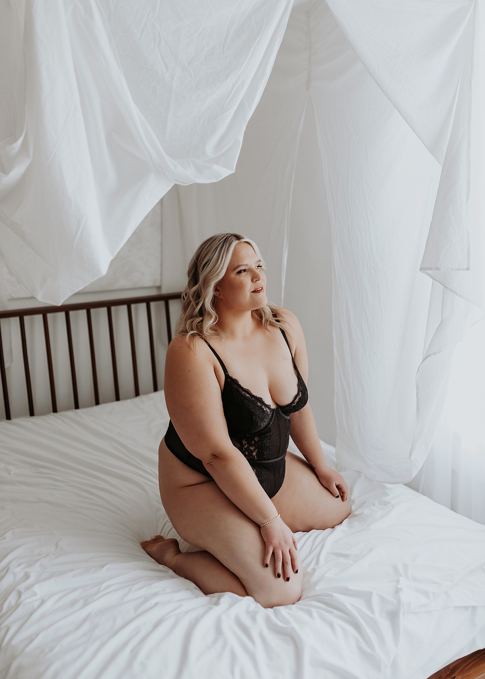 Blonde woman in sheer bodysuit lingerie on a white bed in Minneapolis 