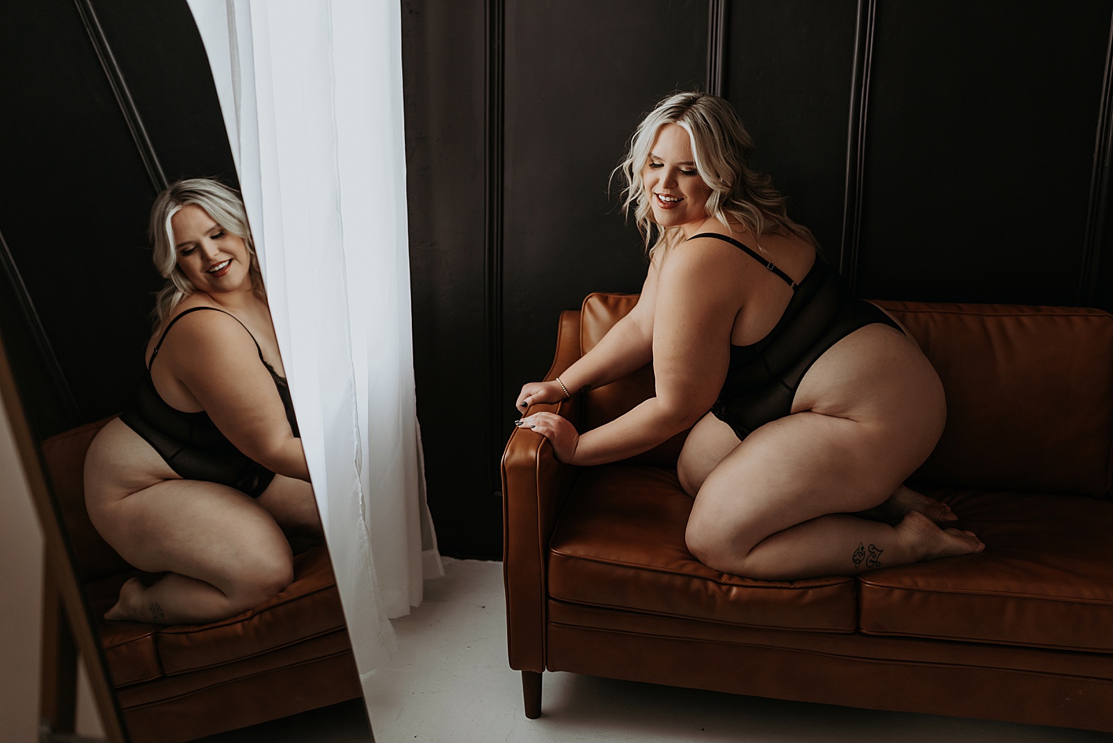 Woman kneeling on leather couch in sheer bodysuit lingerie at boudoir studio in Minnesota 