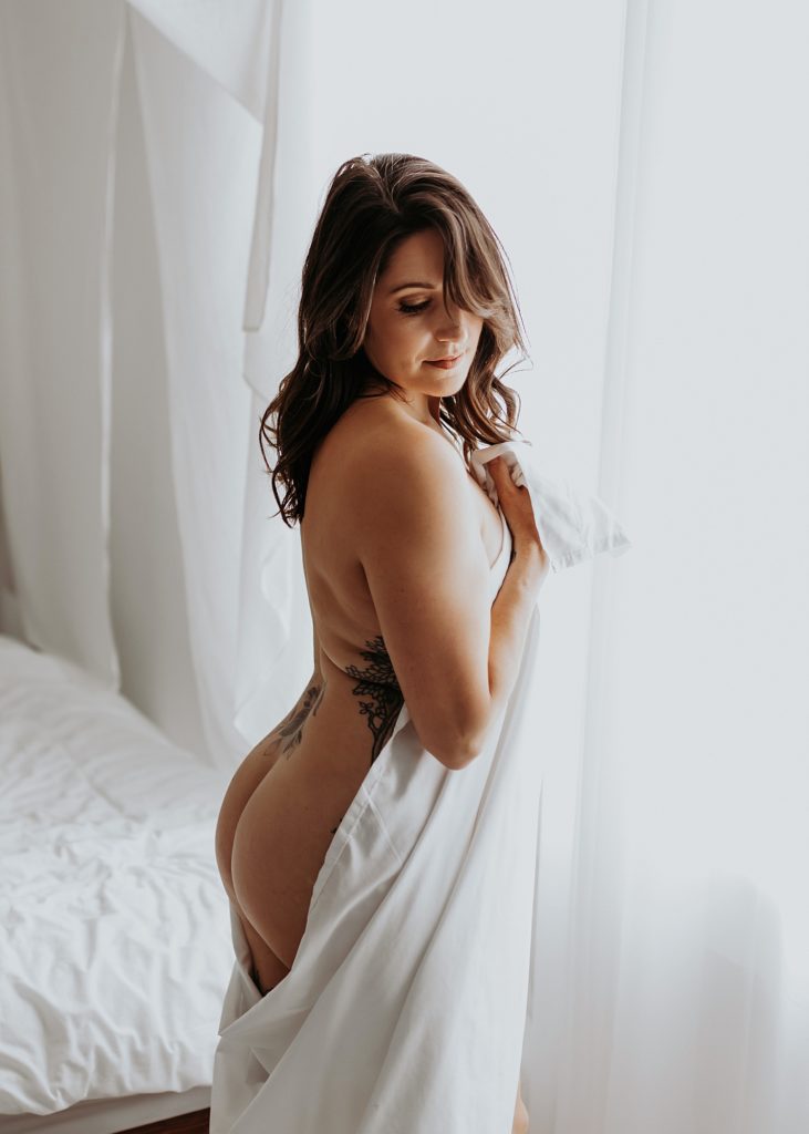 nude woman covering herself with a sheet for boudoir session 