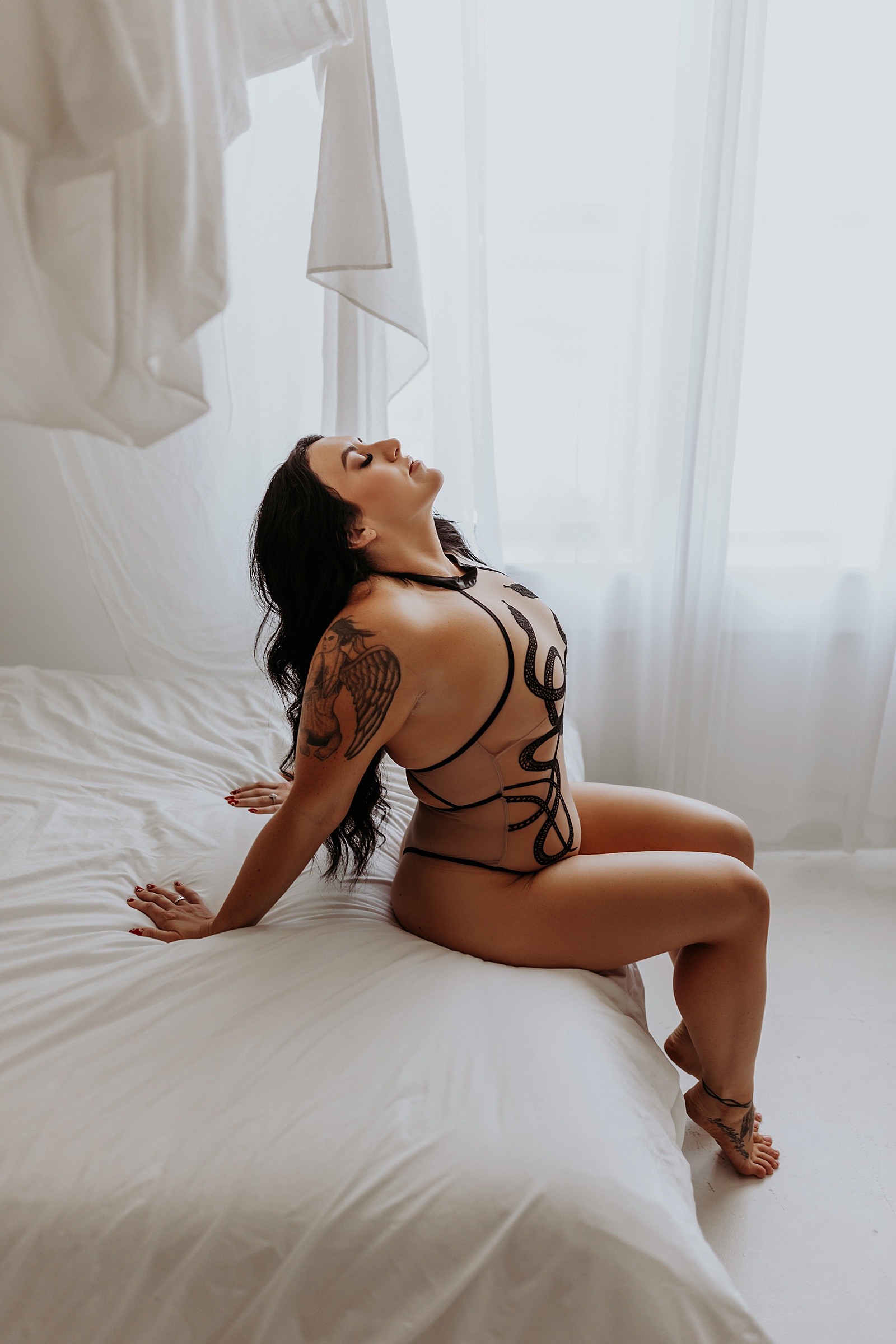 Brunette woman leaning back on a white bed wearing a thistle & spire bodysuit