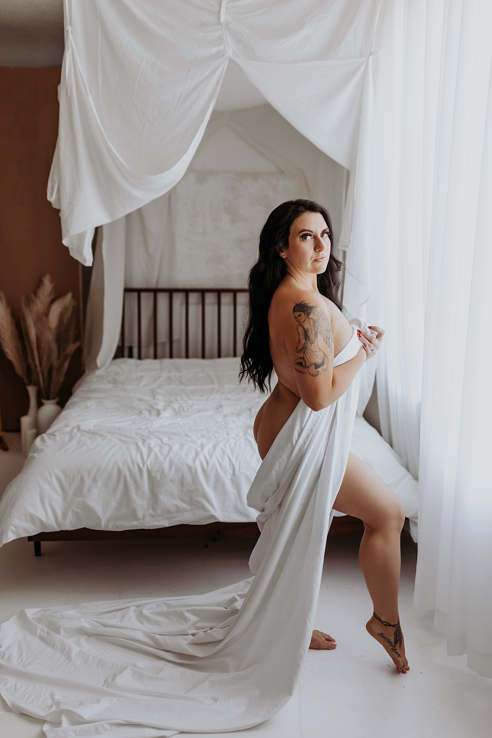 Brunette with tattoos naked in front of a window covered with a sheet 
