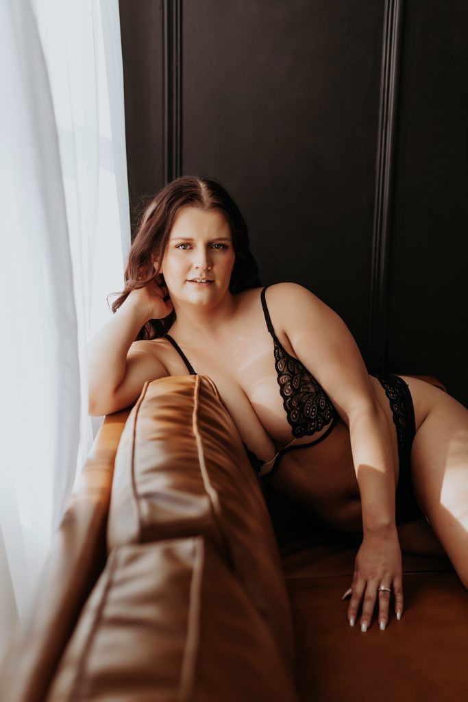 Brunette in black two piece lingerie sitting on a leather couch by a Minneapolis boudoir photographer 