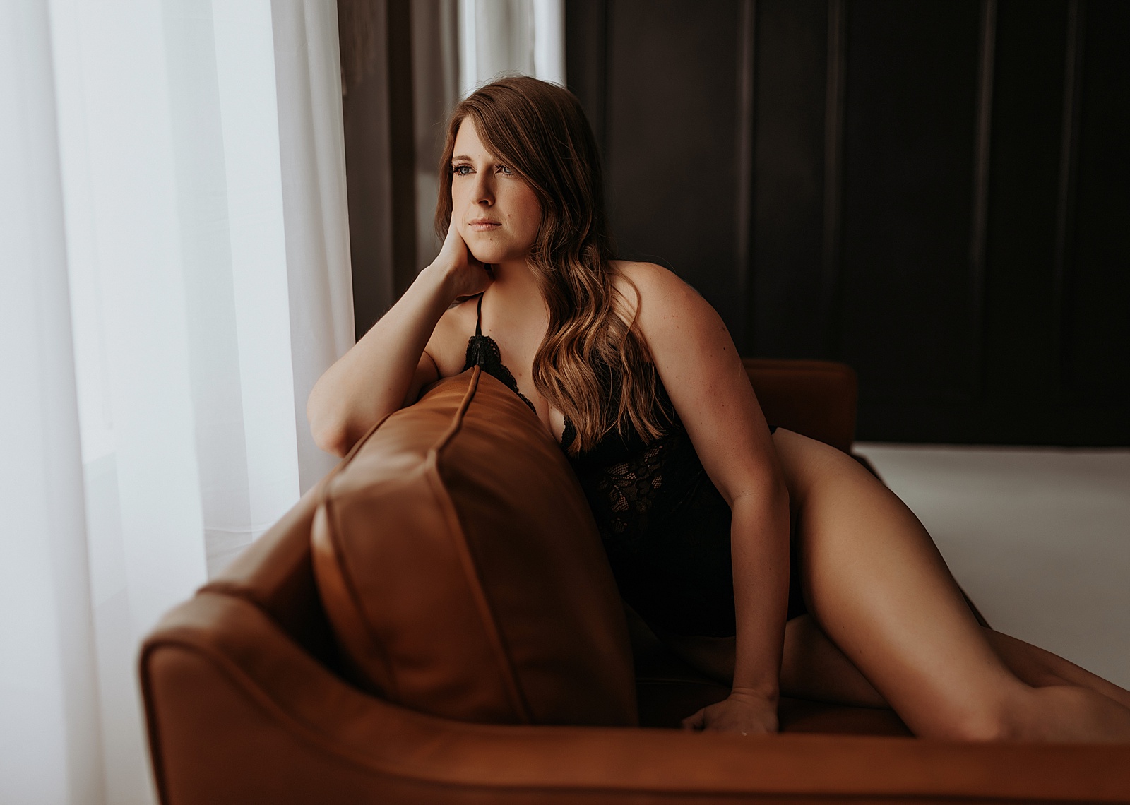 Brunette sitting on a leather couch looking at out the window by Mary Castillo Photography 
