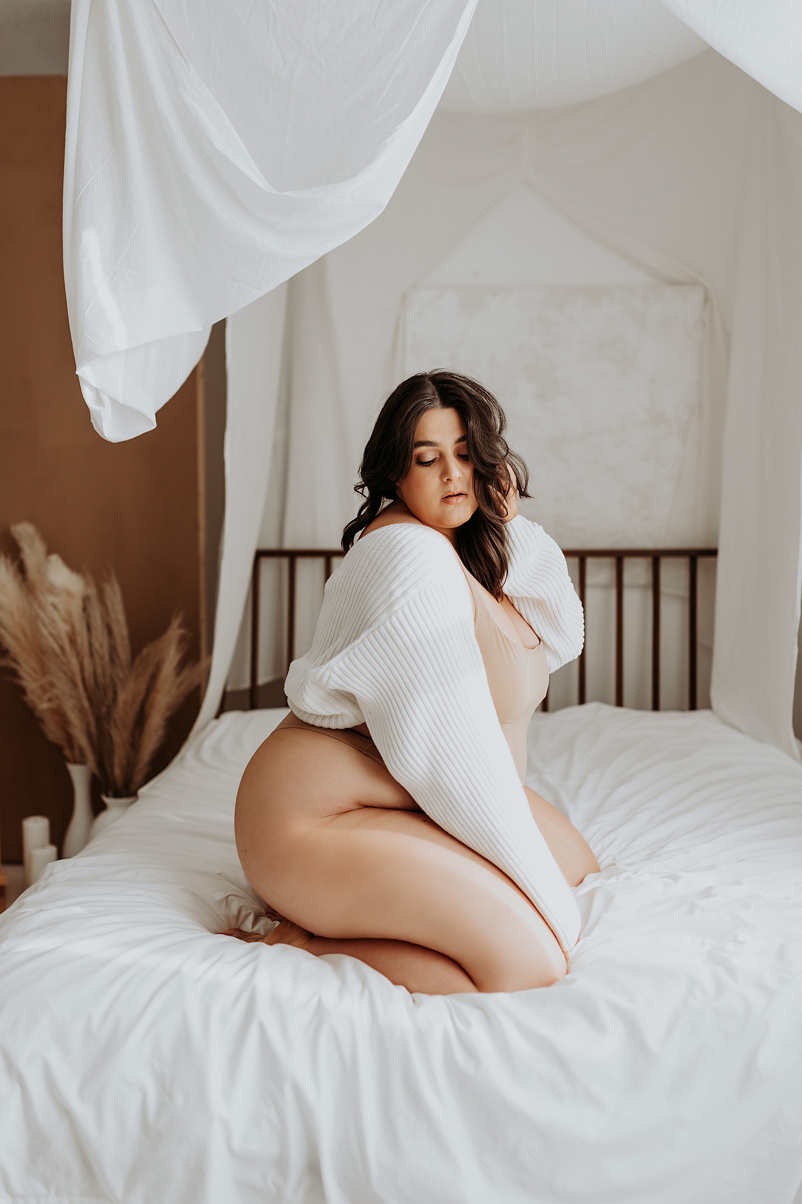 Brunette in nude bodysuit kneeling on studio bed by Mary Castillo Photography