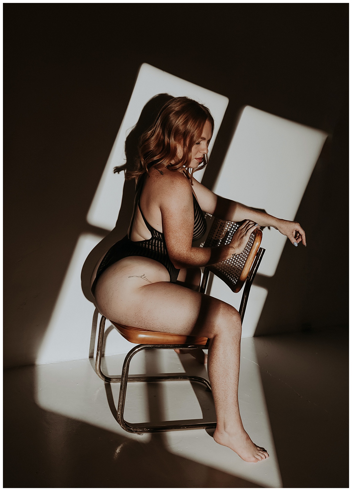 Person sits on chair in front of light in Black Sheer Bodysuit