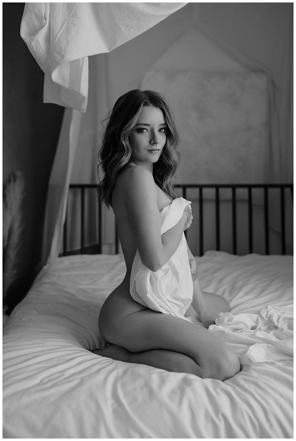 Female sits on bed covering body with sheet for Minneapolis Boudoir Photographer