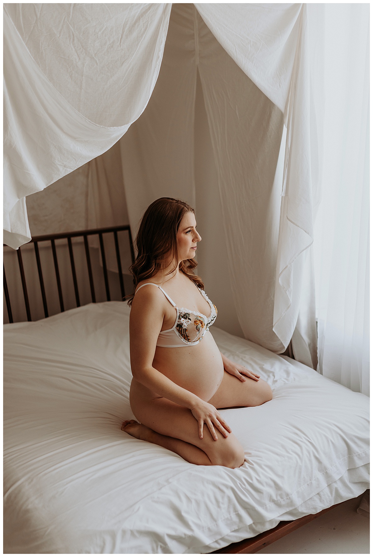Mama sits on bed in white lingerie for Maternity Boudoir session