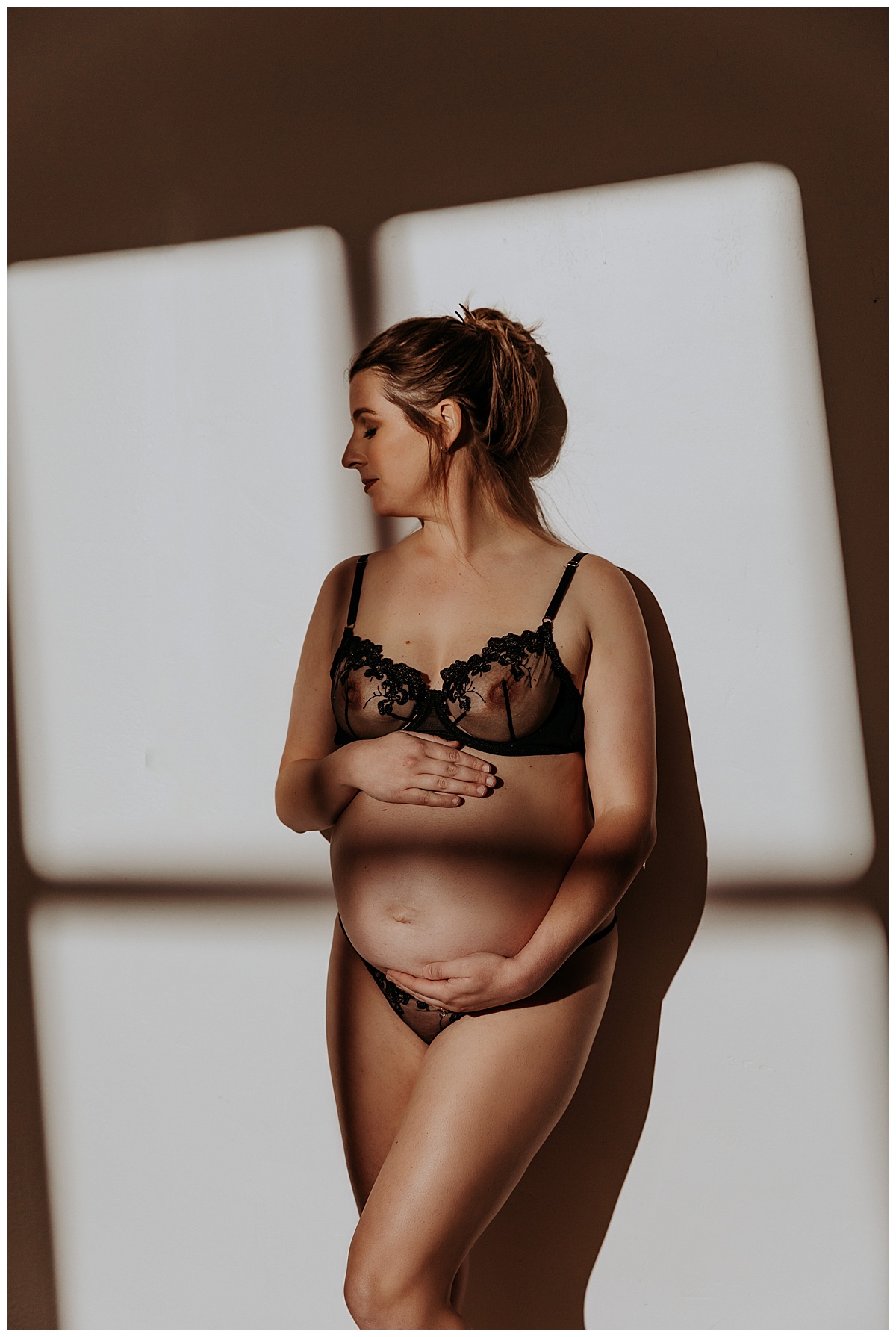 Pregnant Woman looks over shoulder and grabs pregnant belly in black lingerie for Mary Castillo Photography