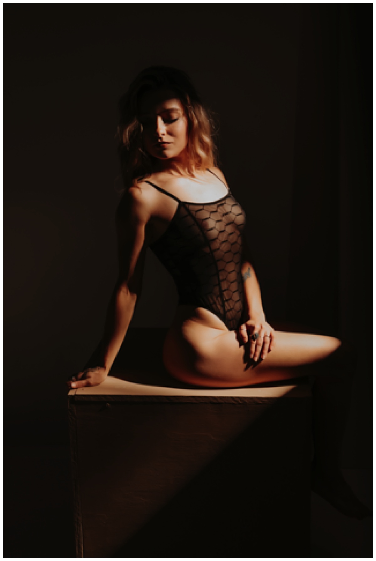 Female sits down wearing black lingerie bodysuit for Mary Castillo Photography