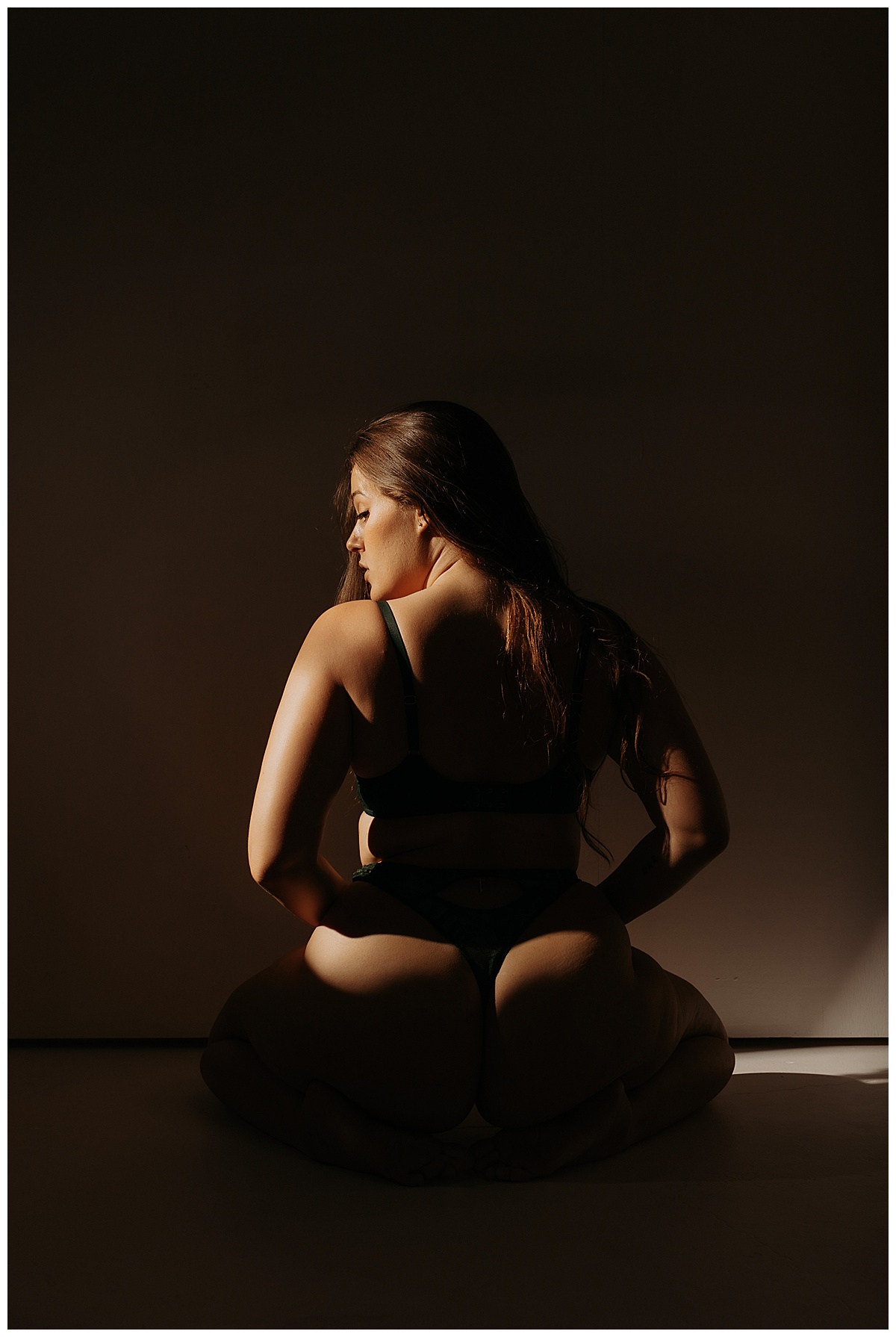 Person kneels in lingerie using artificial light during boudoir session