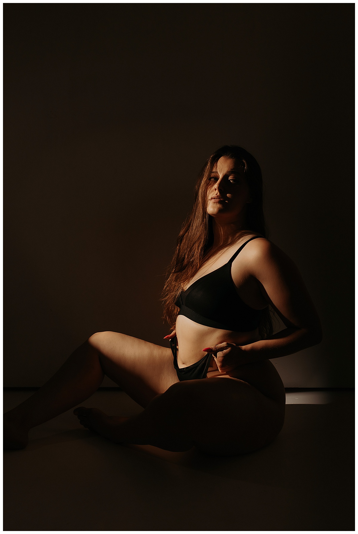 Girl adjusts lingerie bottoms using artificial light during boudoir session