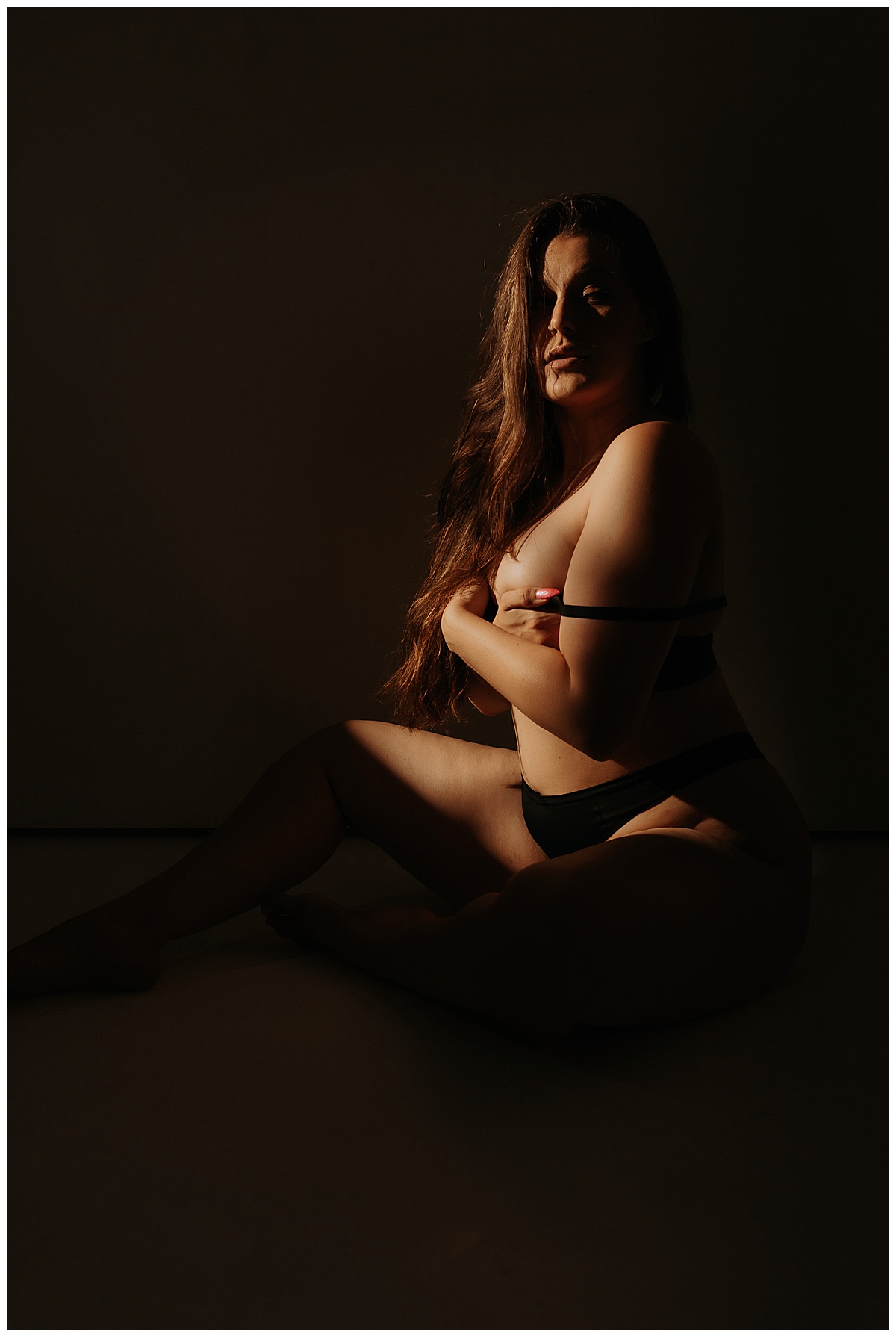 Lady covers chest with lingerie and hands using artificial light during boudoir session