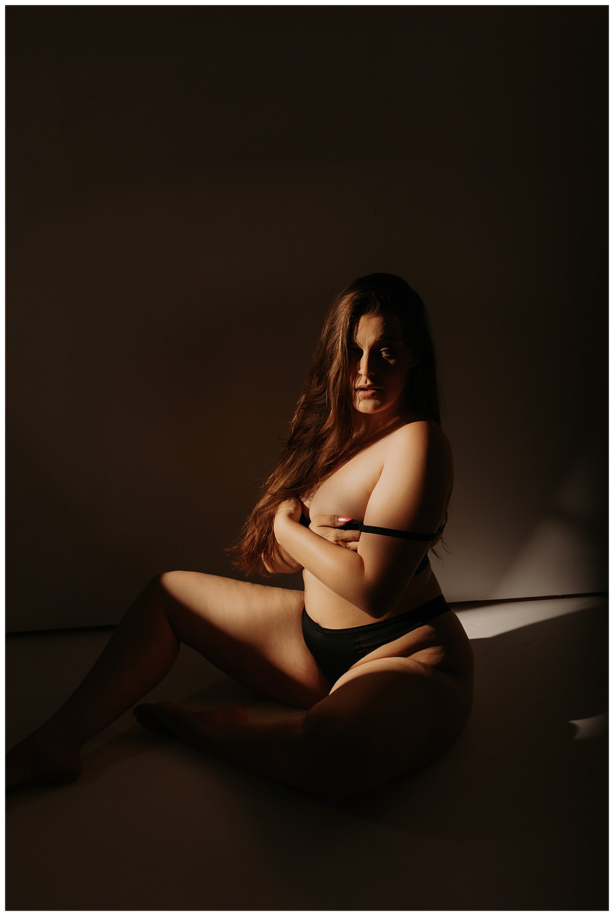 Female covers body using artificial light during boudoir session