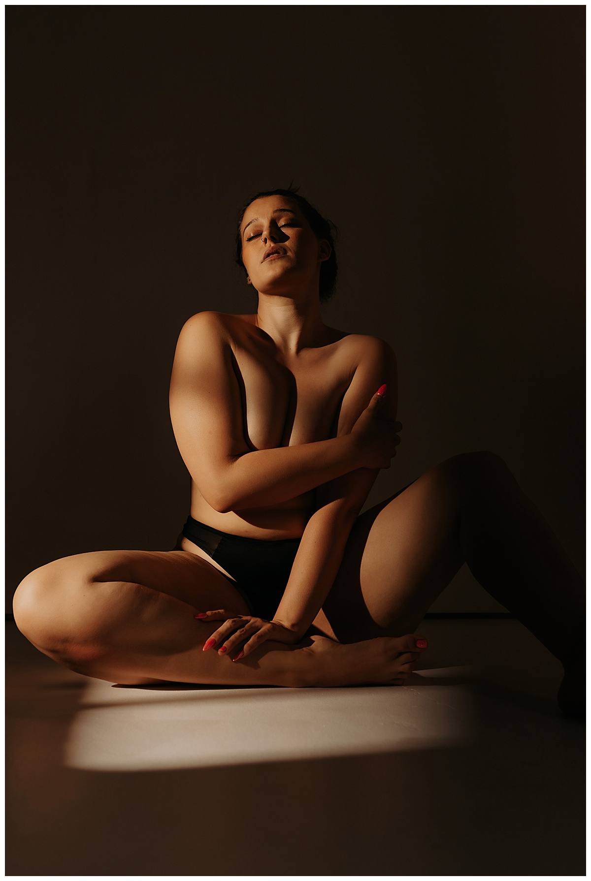 Adult covers body and sits down using artificial light during a boudoir session