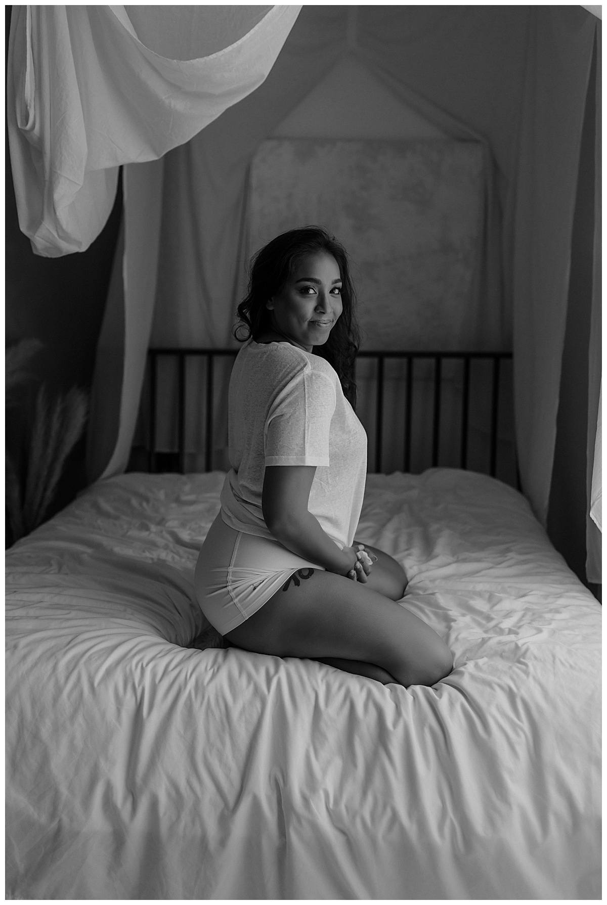 Female sits on the bed wearing a shirt for Minneapolis Boudoir Photographer