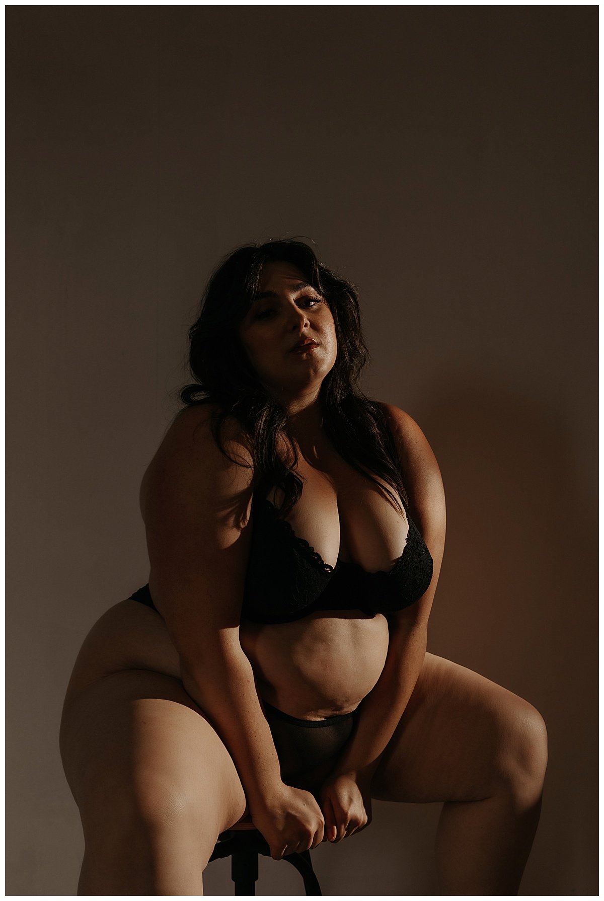 Woman sits on the stool and leans forward wearing lingerie in the Studio Lighting