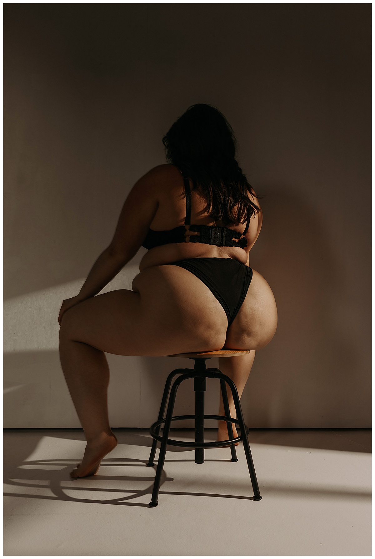 Woman sits on the stool in black lingerie in the Studio Lighting