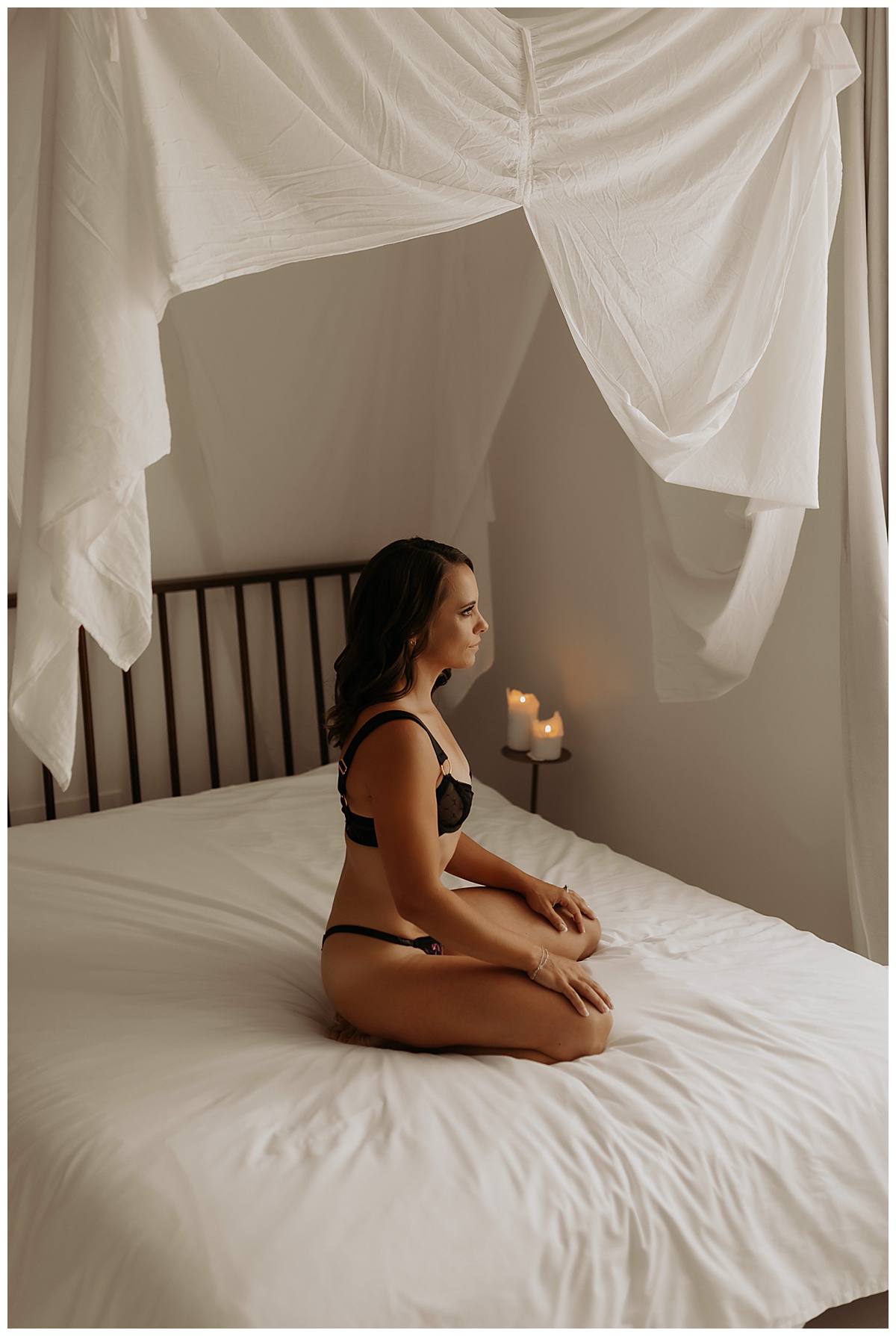 Woman sits on the bed in black lingerie for Birthday Boudoir Session