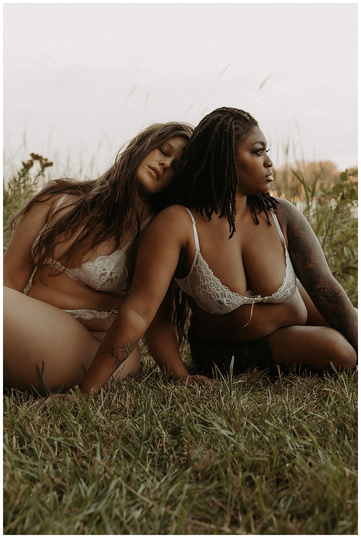Two adults sit on the grass in white lingerie for their outdoor boudoir session