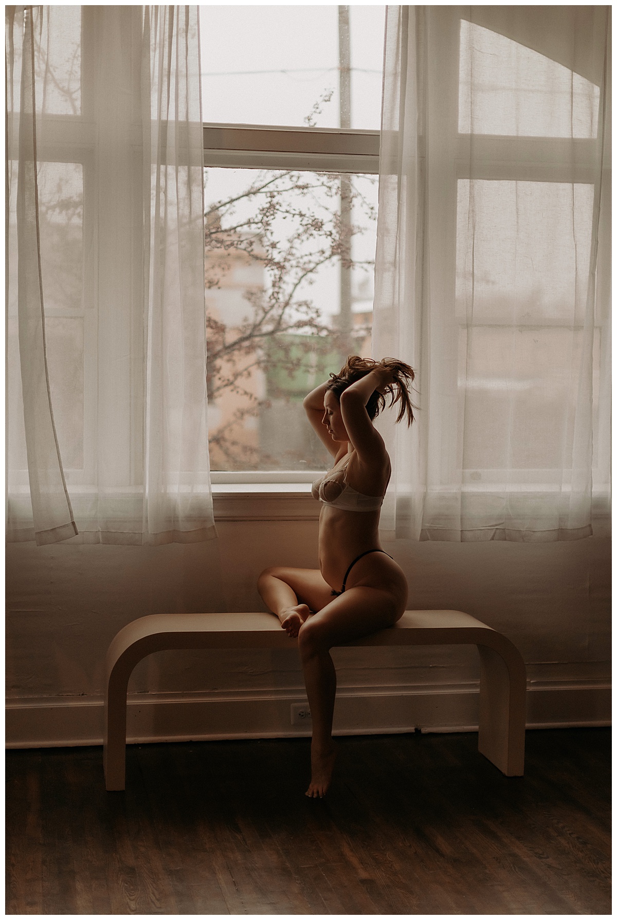 Adult holds her hair up in front of a window showing Why You Should Book A Boudoir Session in 2024