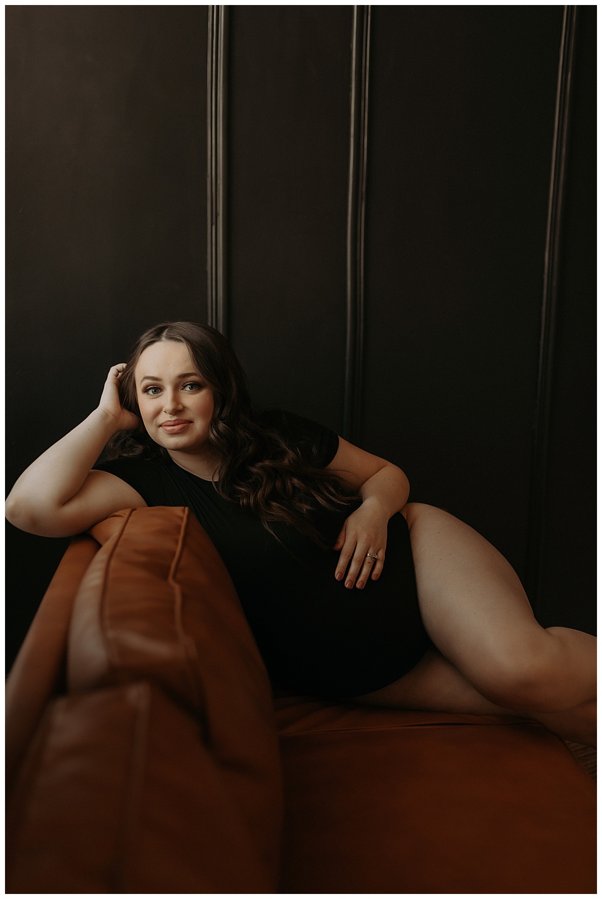 Adult lays on the couch wearing a black bodysuit for Minneapolis Boudoir Photographer