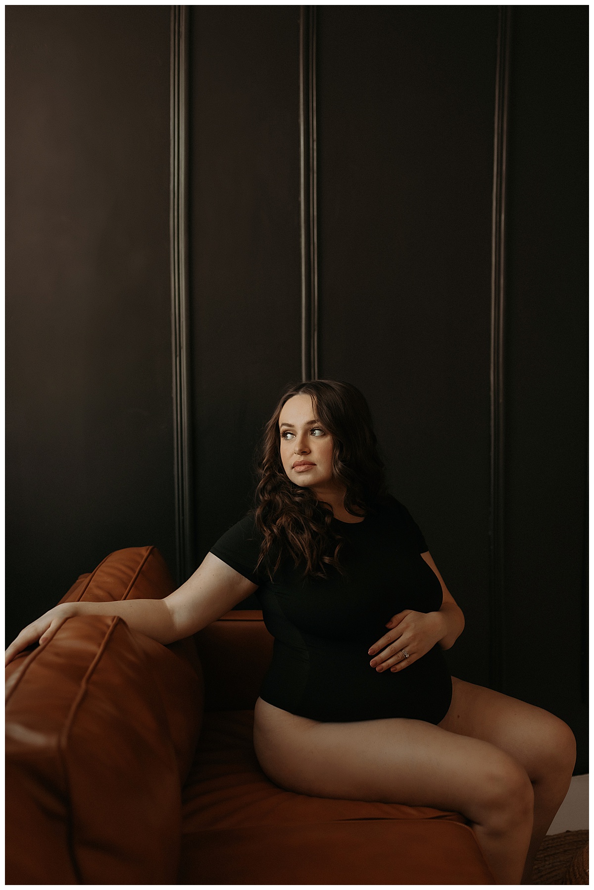 Mom sits on the couch looking out the window and holds baby bump for Mary Castillo Photography