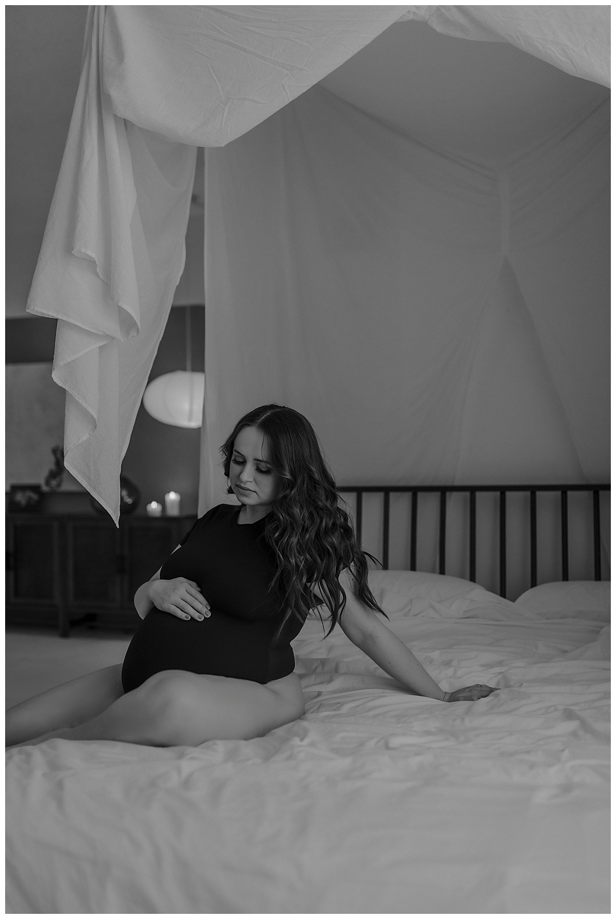Woman sits on the bed holding baby bump for Minneapolis Boudoir Photographer