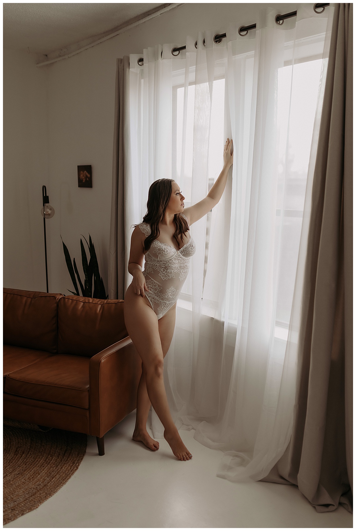 Woman stands in front of a window wearing white lingerie showing the benefits of doing More Than One Boudoir Session