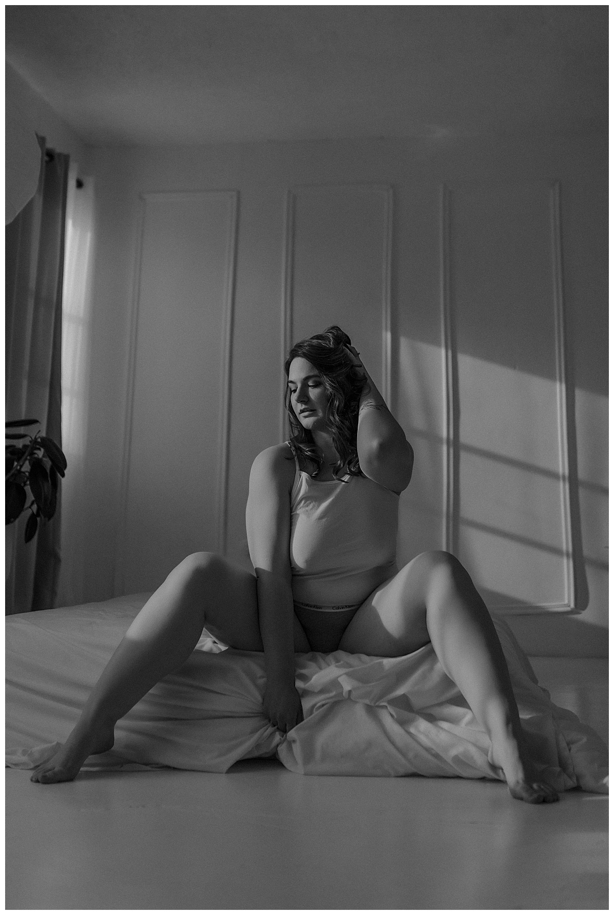 A person sits on the edge of the bed with hand running through her head for Minneapolis Boudoir Photographer
