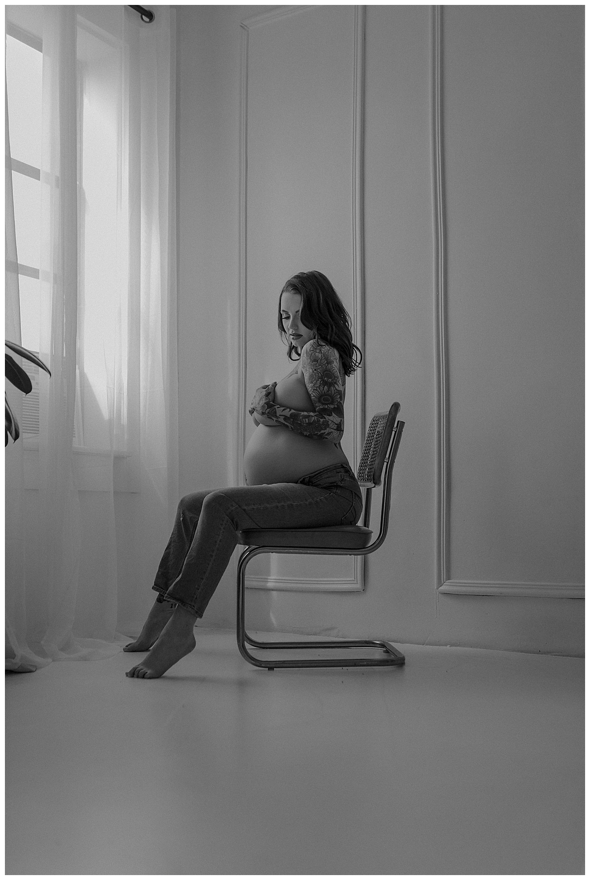 Woman sits in chair cover her chest with her hands during her Maternity Boudoir Session
