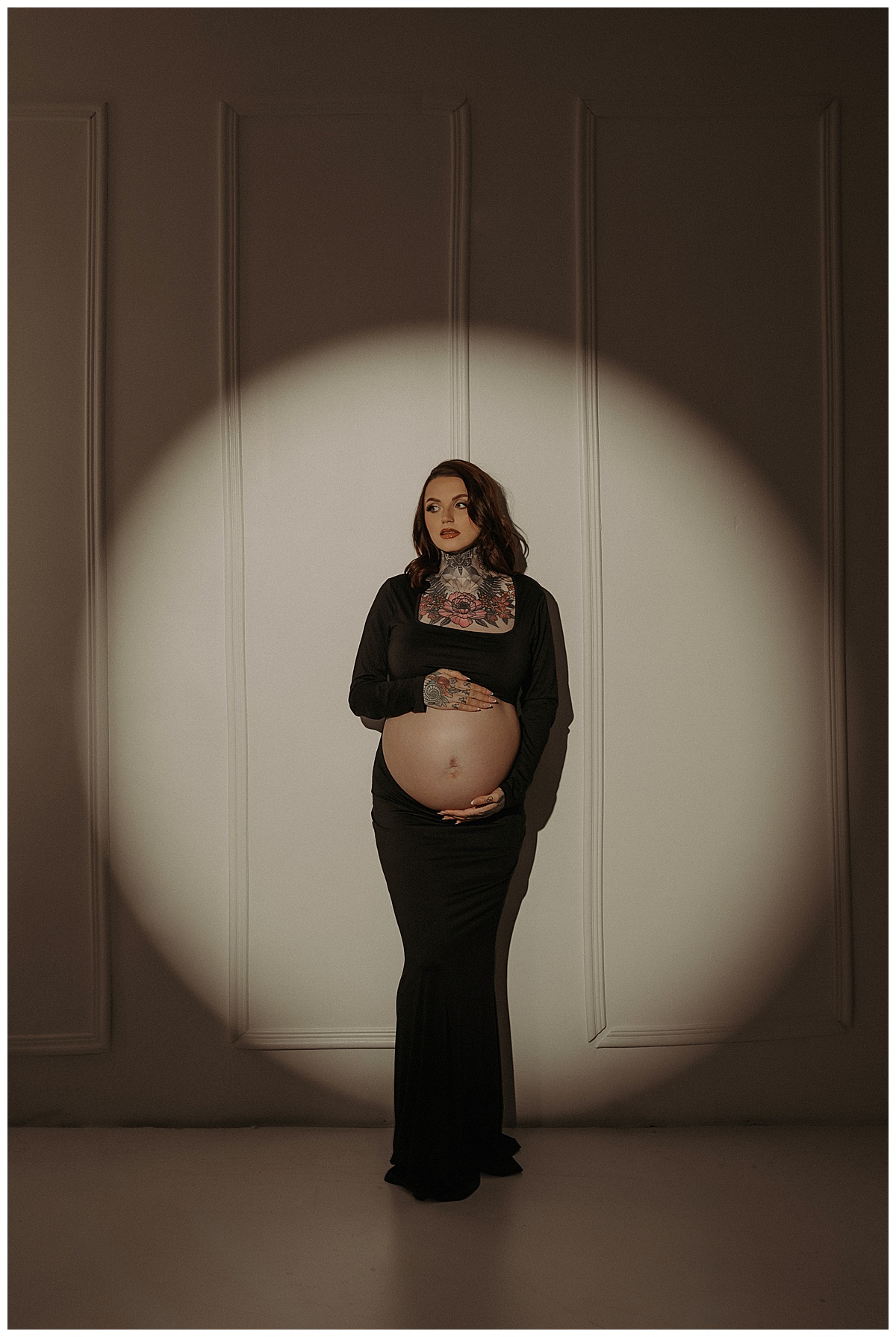 Adult stands in front of spotlight holding her pregnant belly for Mary Castillo Photography