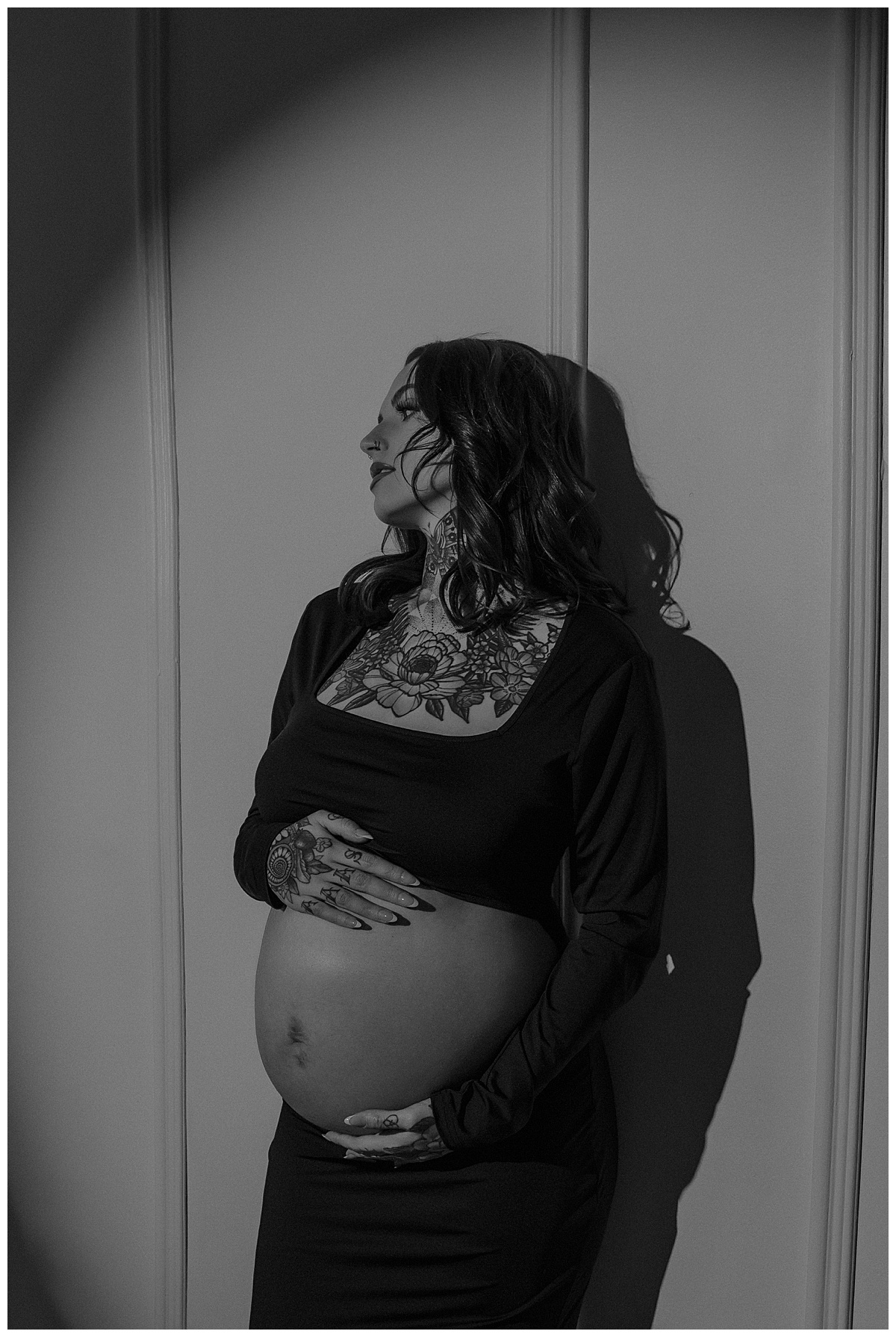 Person stands in front of spotlight holding her pregnant belly during her Maternity Boudoir Session