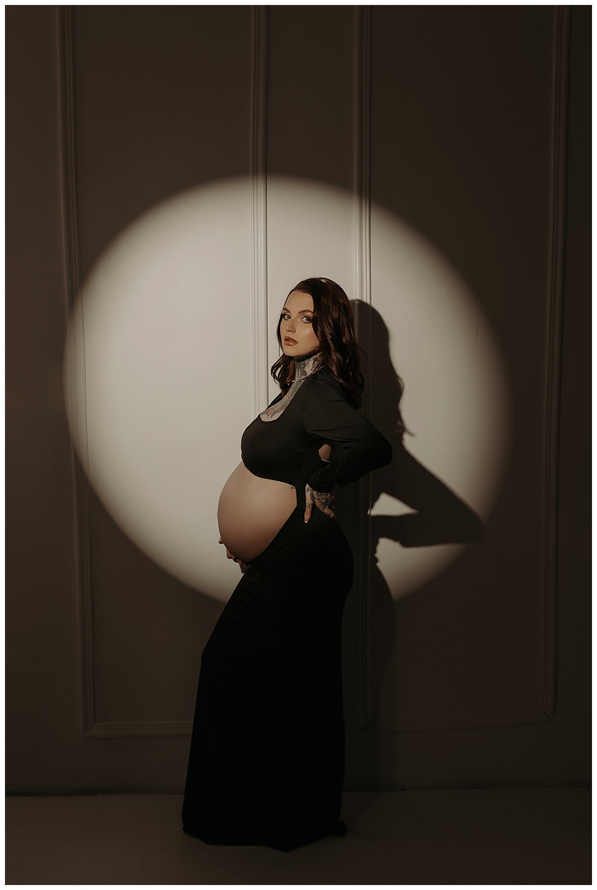 Woman stands in front of spotlight holding her pregnant belly for Mary Castillo Photography