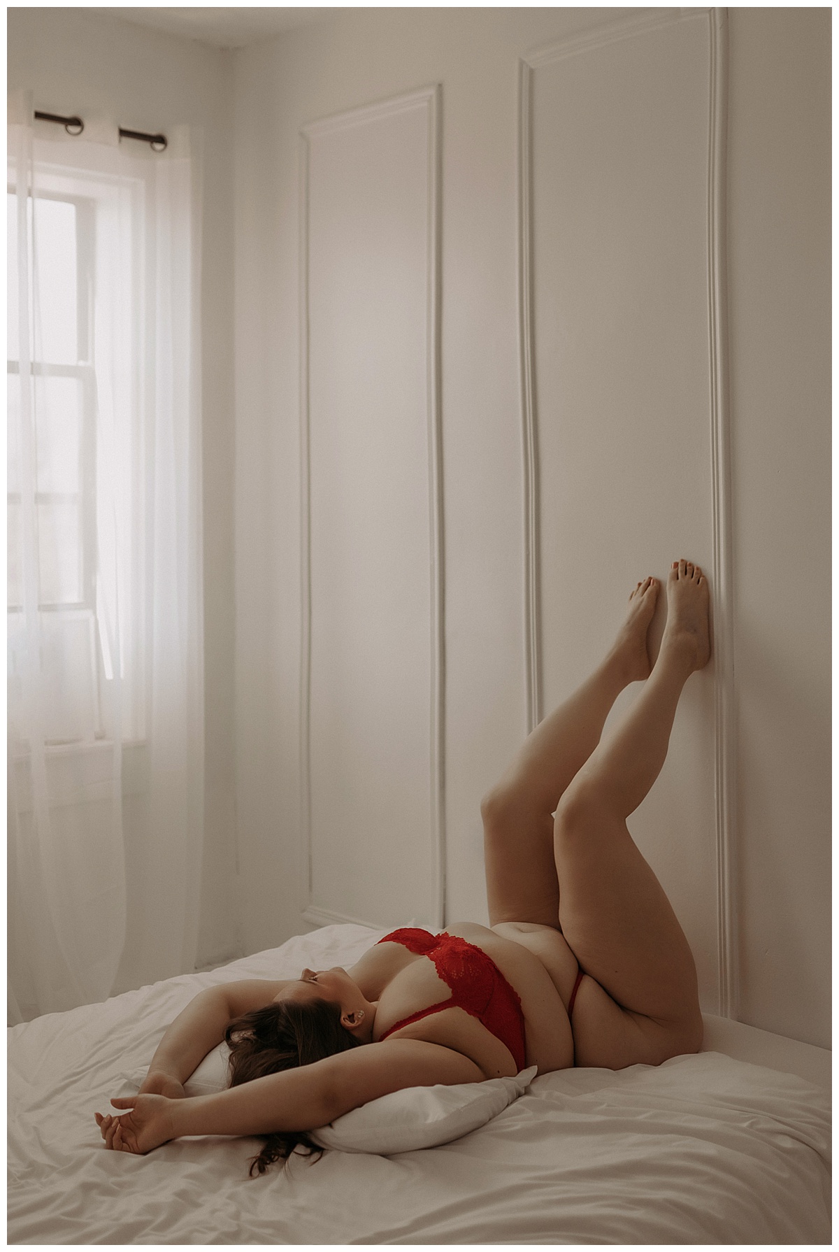 Female lifts her legs against the wall wearing red lingerie for Minneapolis Boudoir Photographer