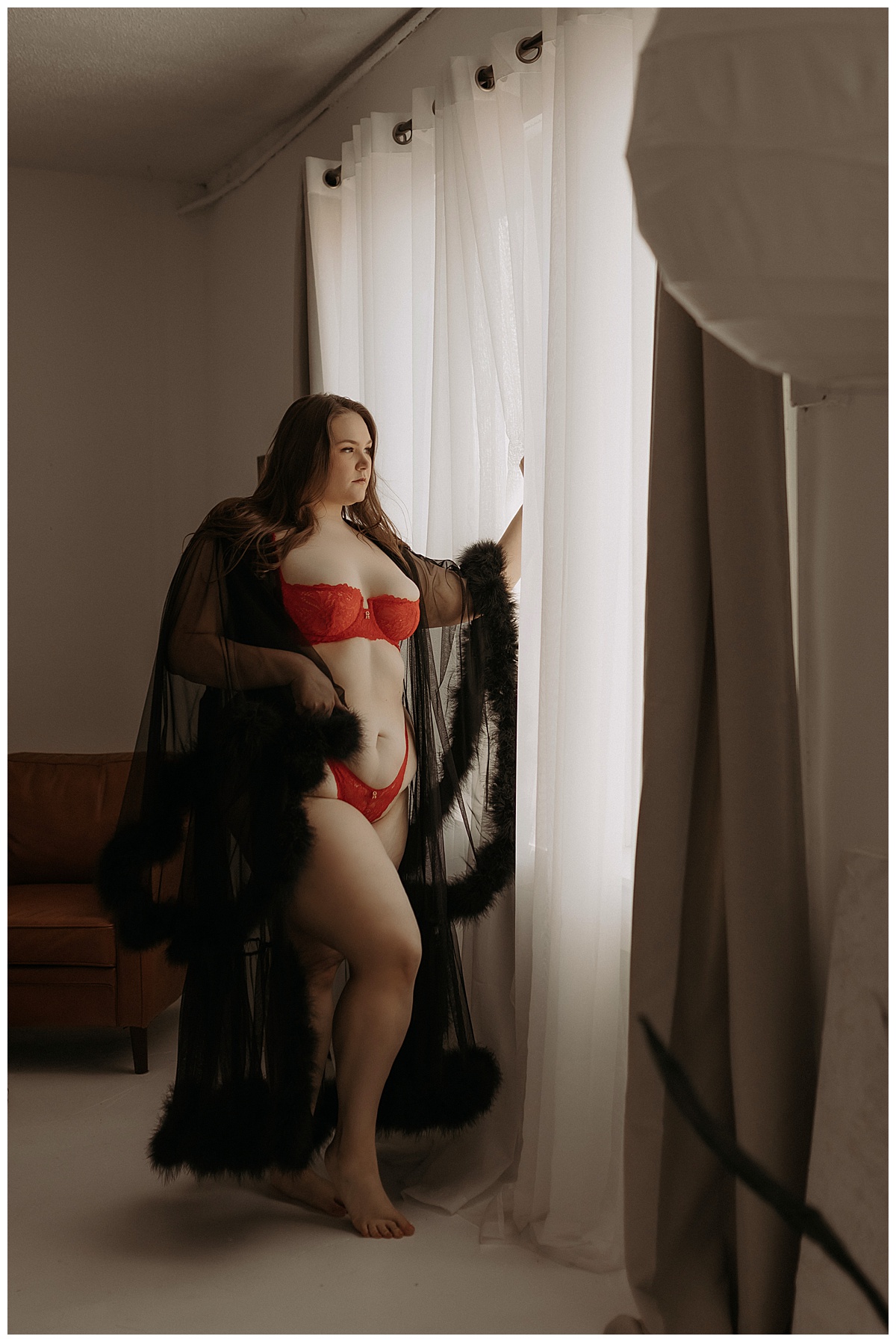 Adult stand in front of a window wearing black lingerie and cover for Minneapolis Boudoir Photographer