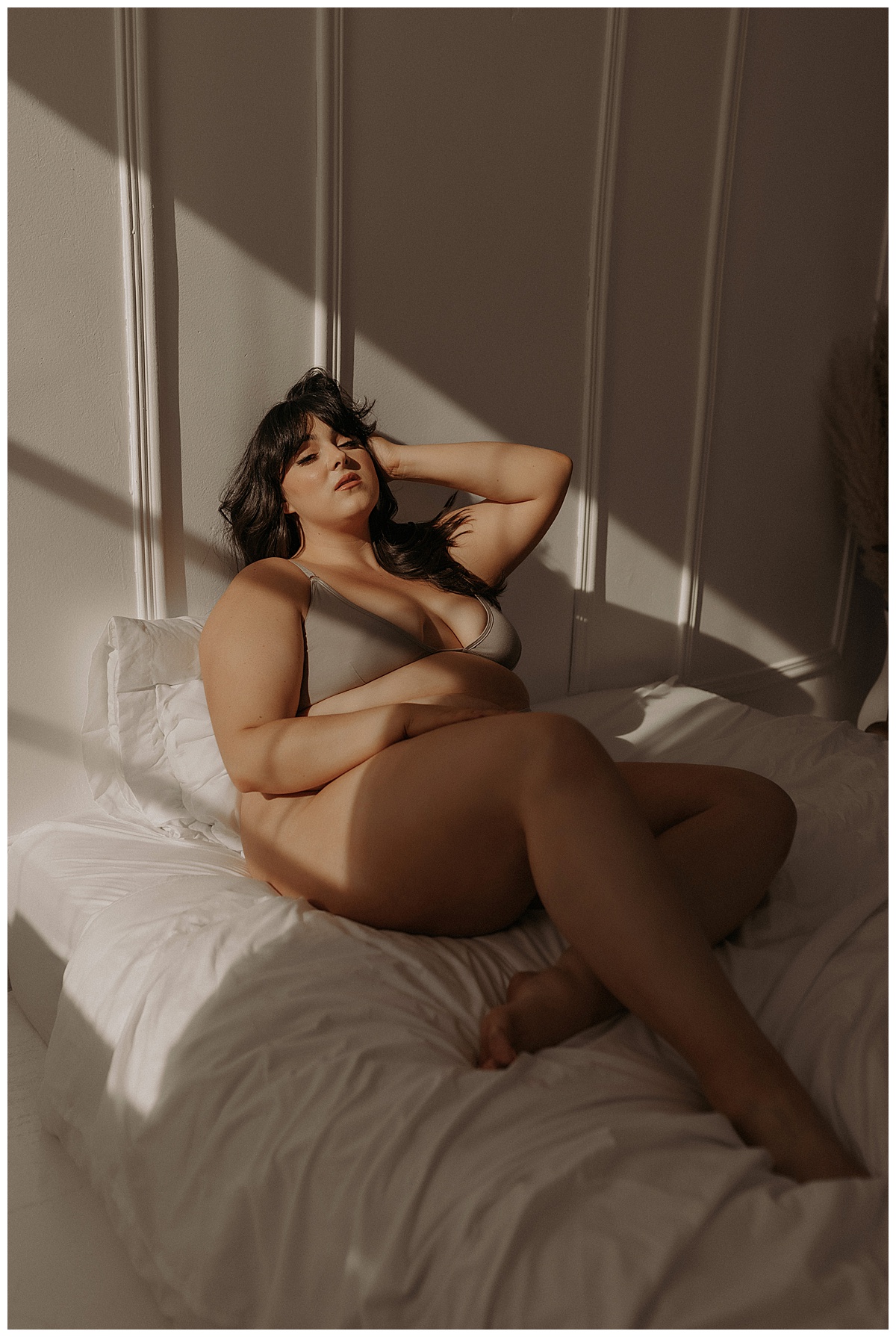 Woman sits on the bed wearing grey lingerie during her Golden Hour Boudoir Session