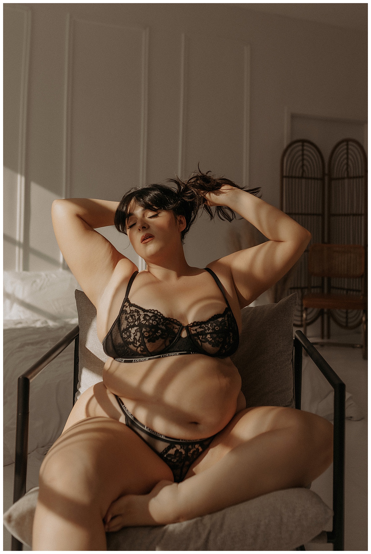 Woman sits on a chair wearing black lingerie during her Golden Hour Boudoir Session