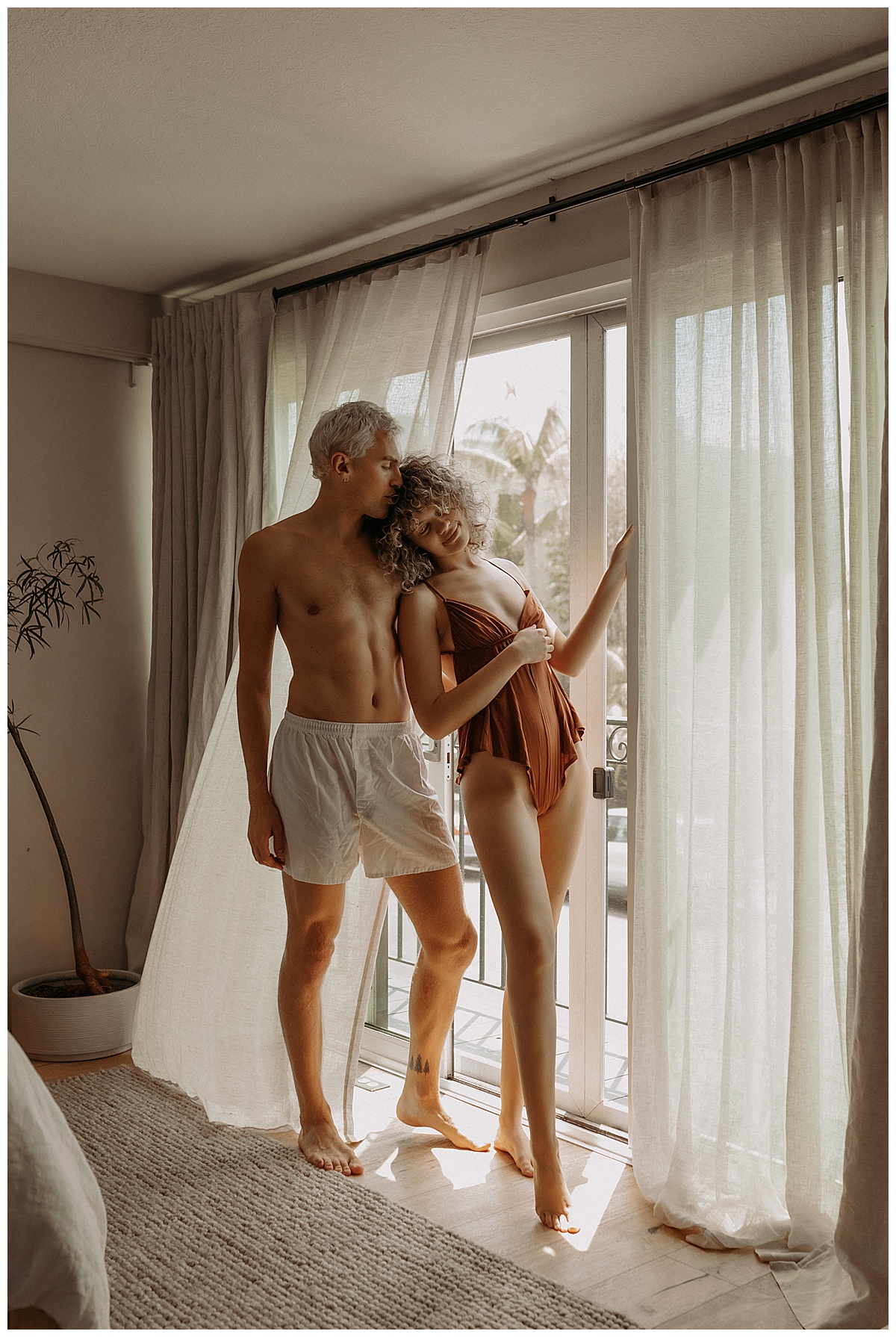 Man and woman stand together in front of window together for Couples Boudoir Session 