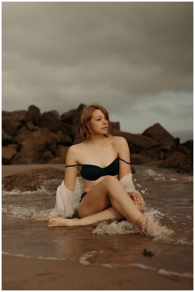 Woman sits on crashing ocean waves showing Why Boudoir Photographers Should Experience A Boudoir Session