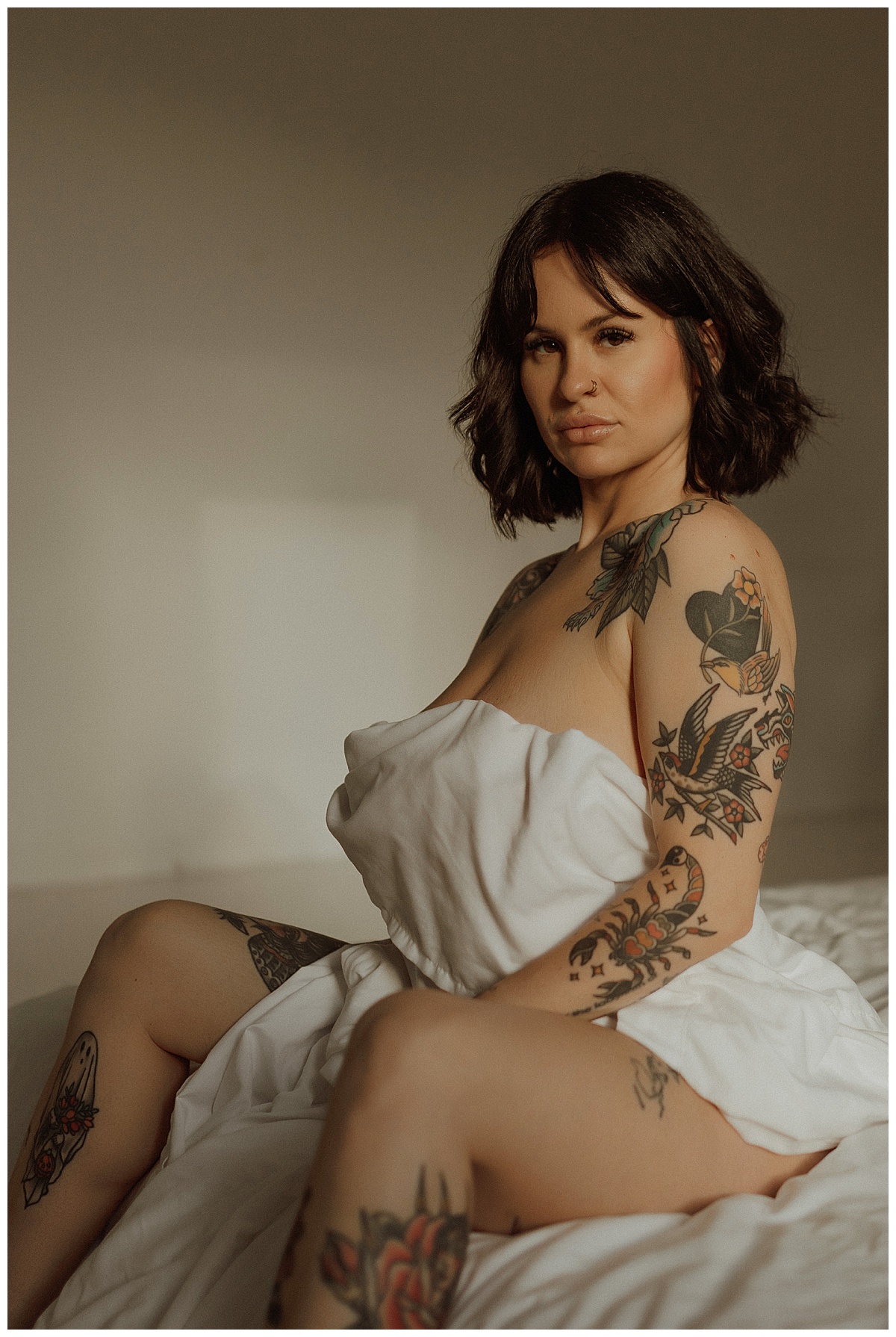 Woman sits on the bed holding a white sheet following What To Expect During Your Boudoir Session