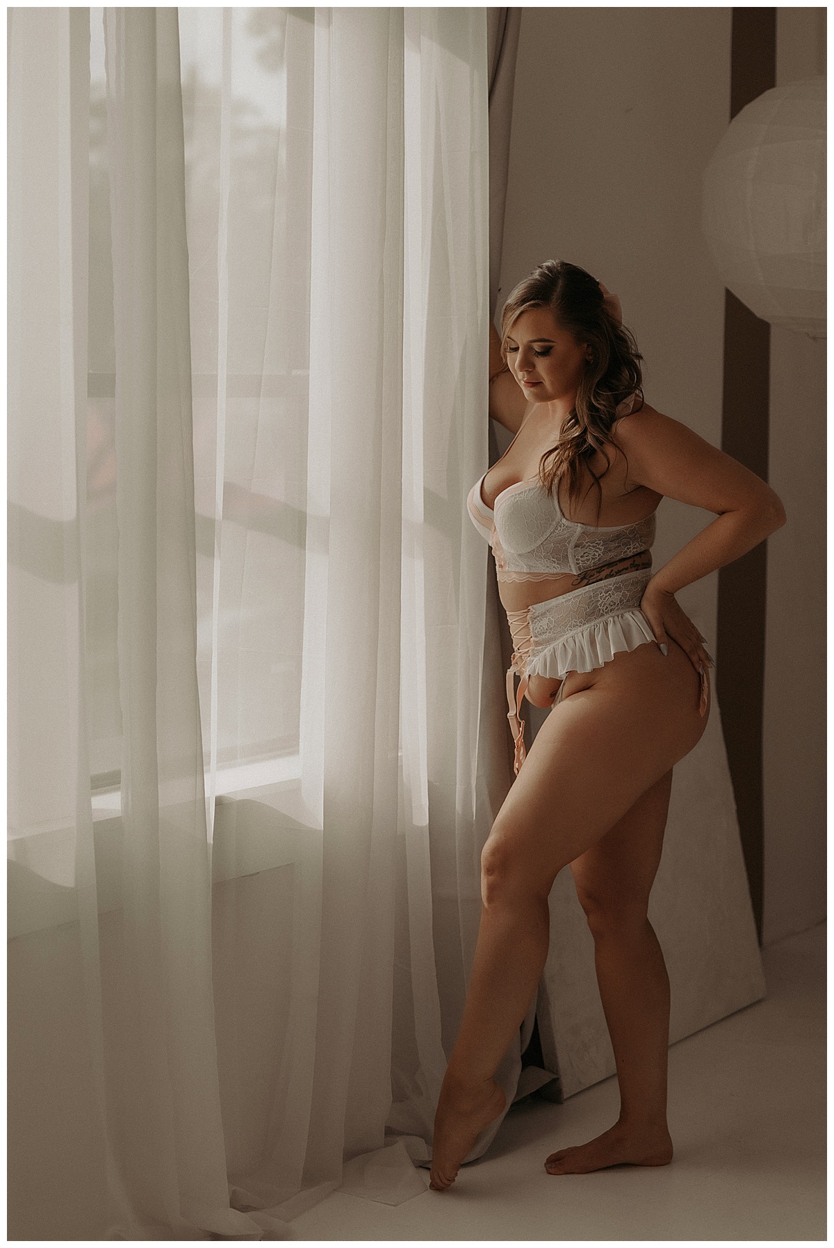 Woman wears white lingerie and stands in front of the window showing Why Boudoir Is More Than Just Pictures 